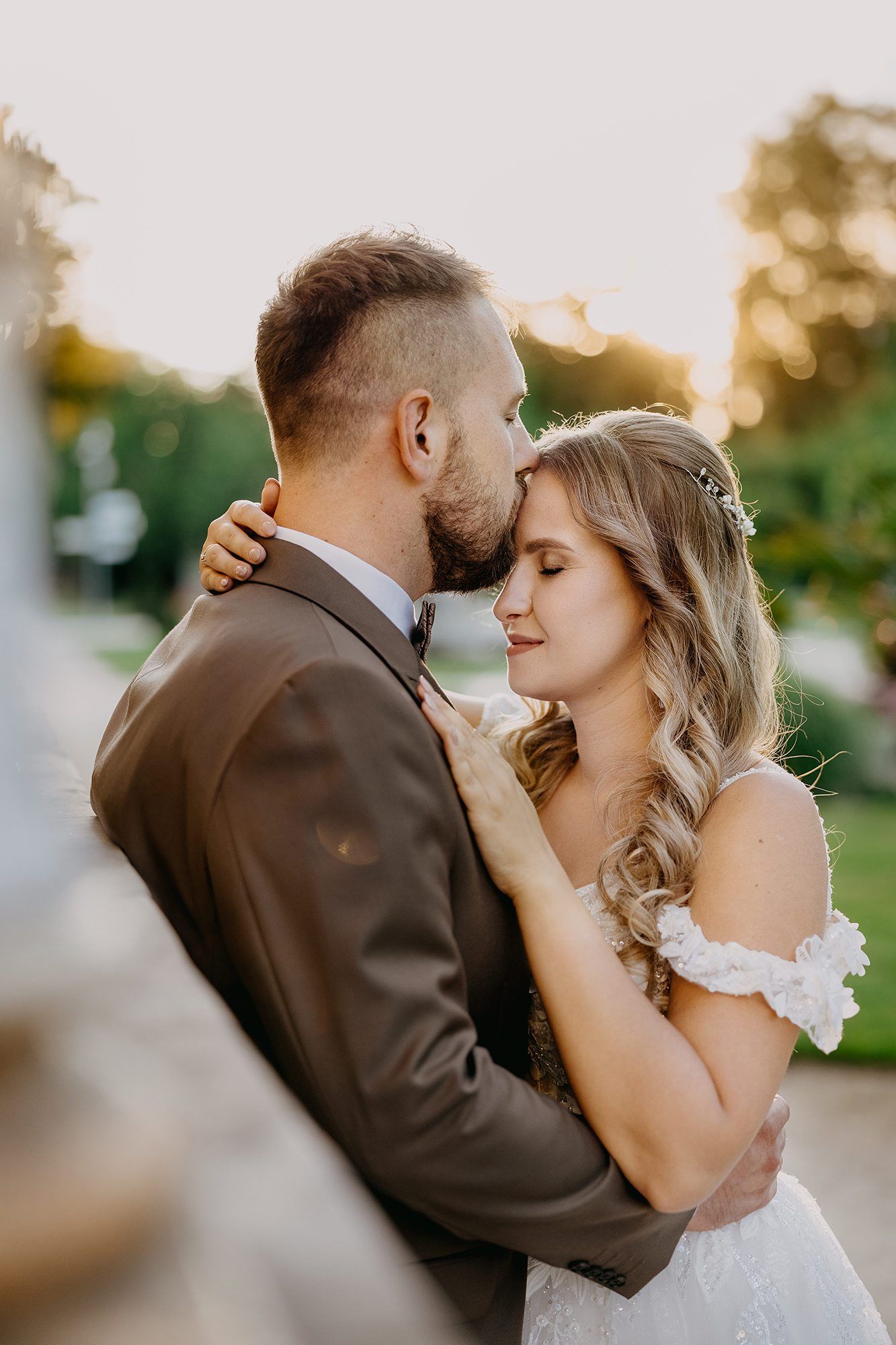 Groom tenderly kissing bride on the forehead during a golden hour outdoor wedding portrait.