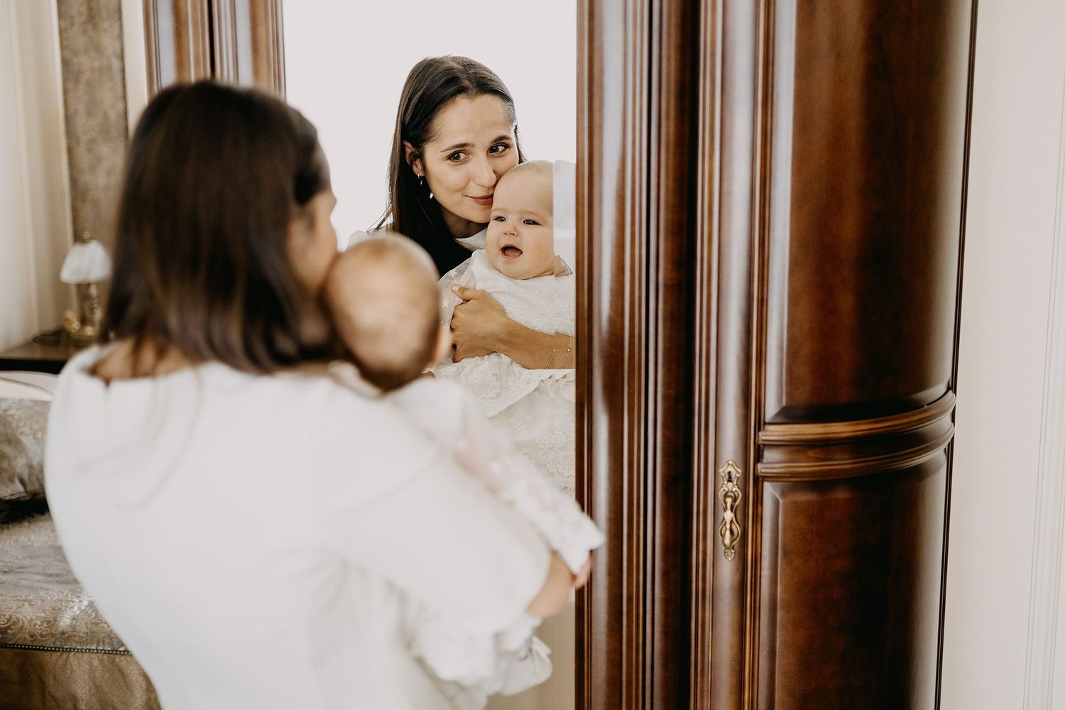 Mother holding her smiling baby while looking at their reflection in a wooden framed mirror.