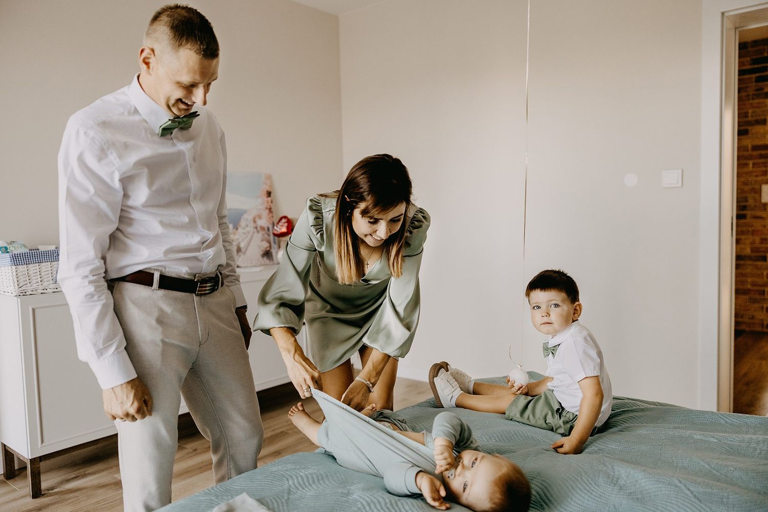 Family with two children preparing baby on bed in bright modern room.