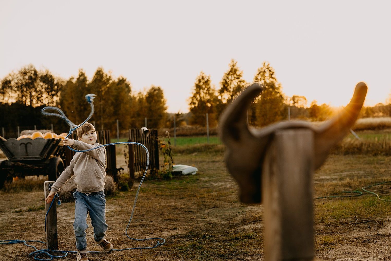 Young child playing near rustic farm equipment at sunset on an autumn farm.