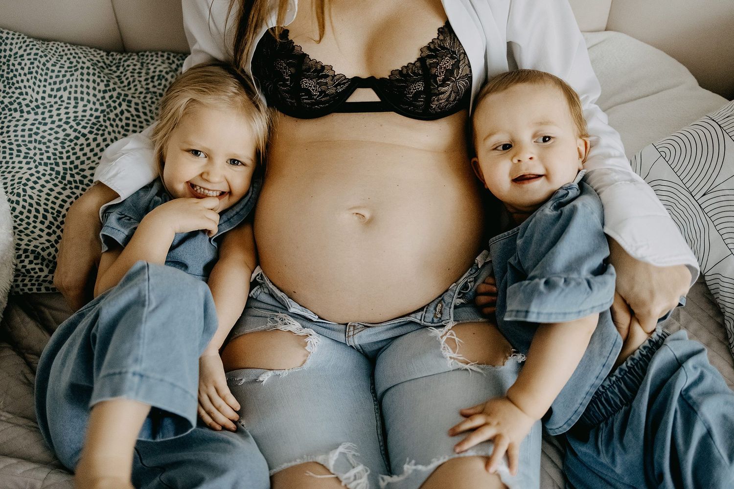 Pregnant mother in black bra sitting with two young children leaning against her bump.