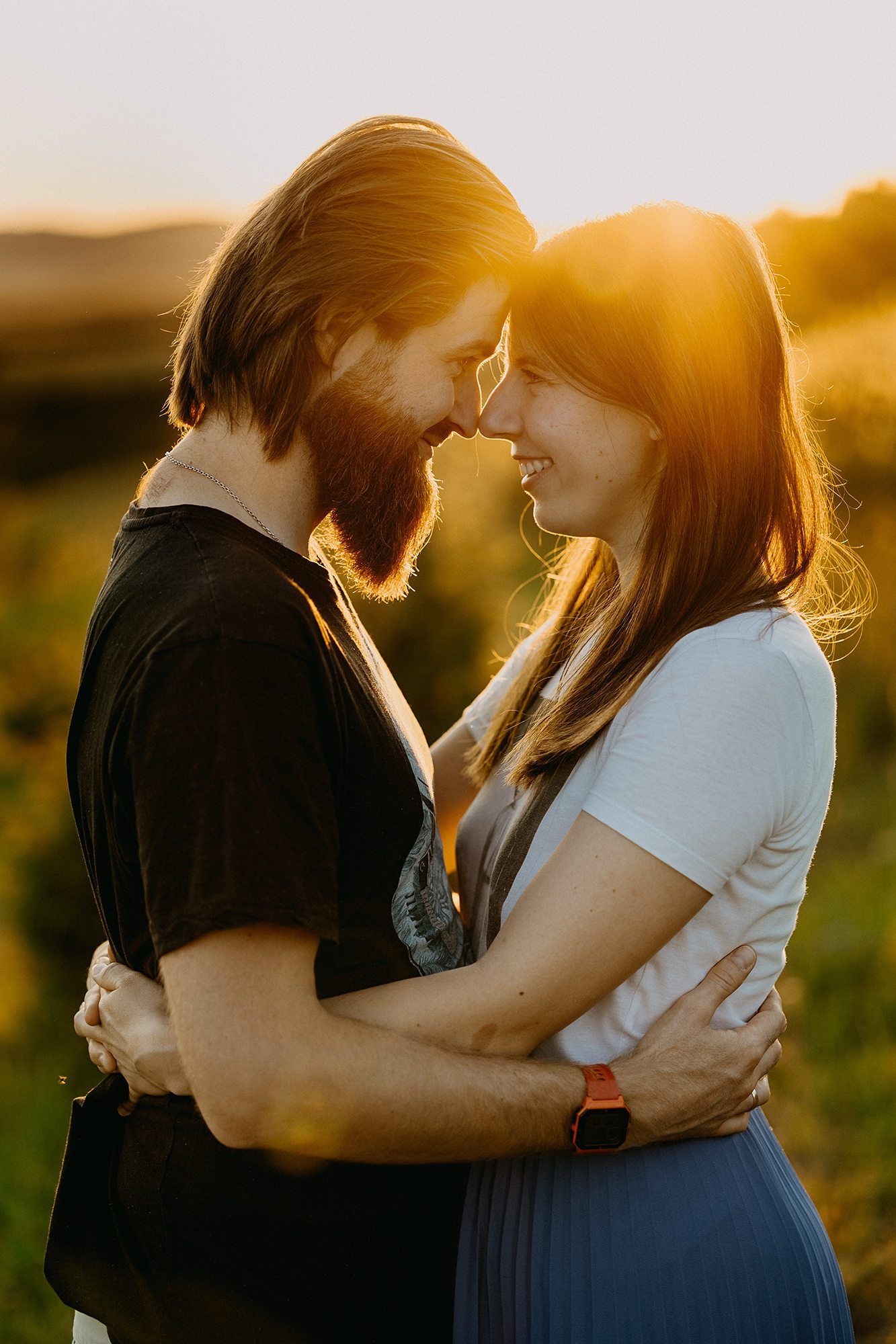 Romantic couple embracing face to face in golden sunset light in an outdoor field setting.