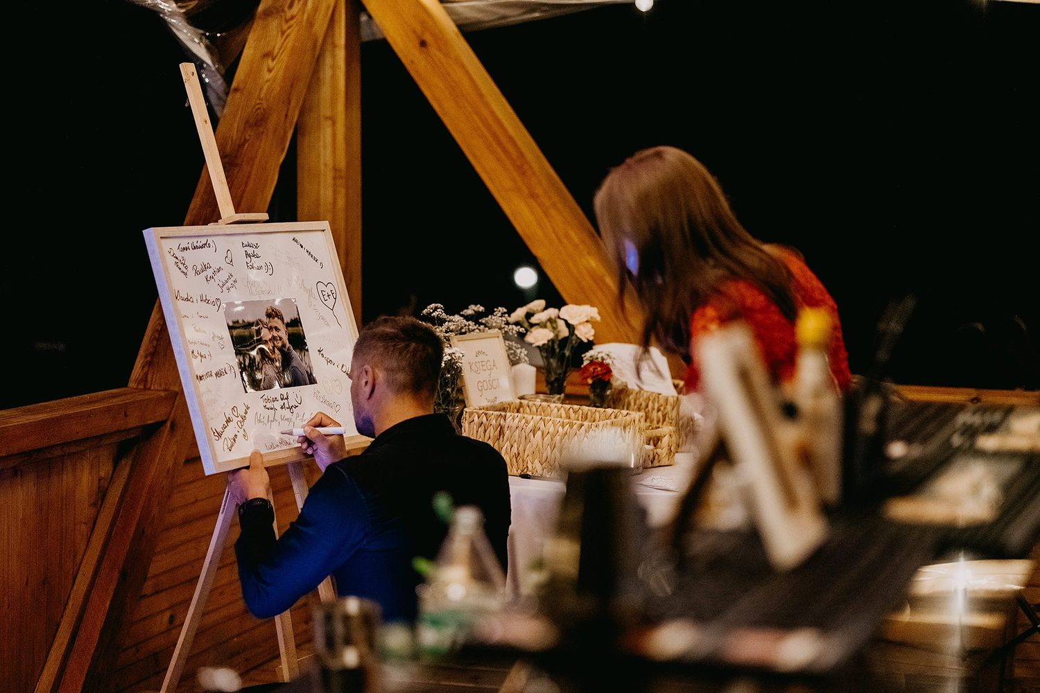 Wedding guest signing a decorative guestbook canvas with couple photo at rustic venue.