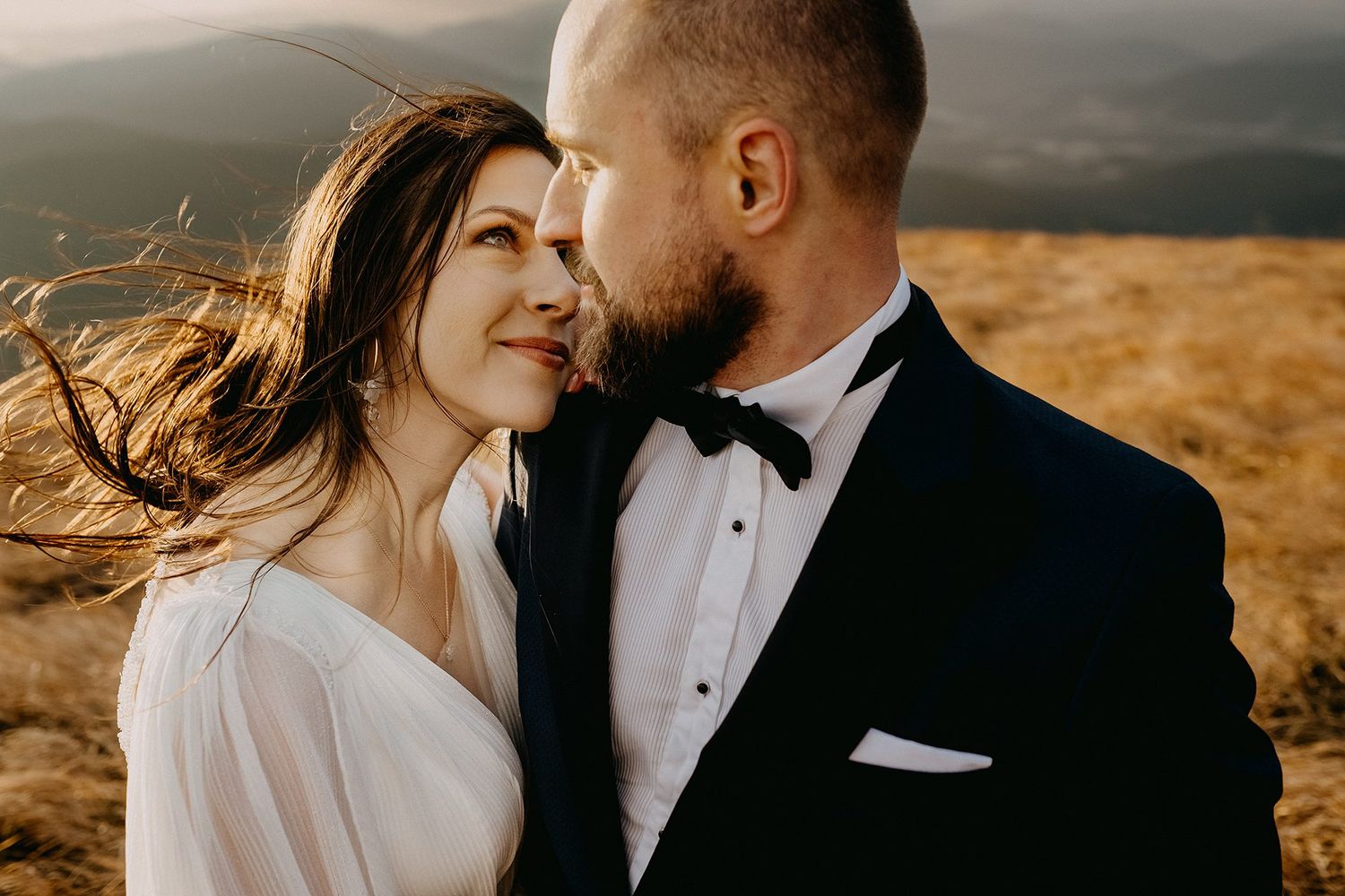 A bride and groom share an intimate moment at golden hour on a scenic mountain hilltop.