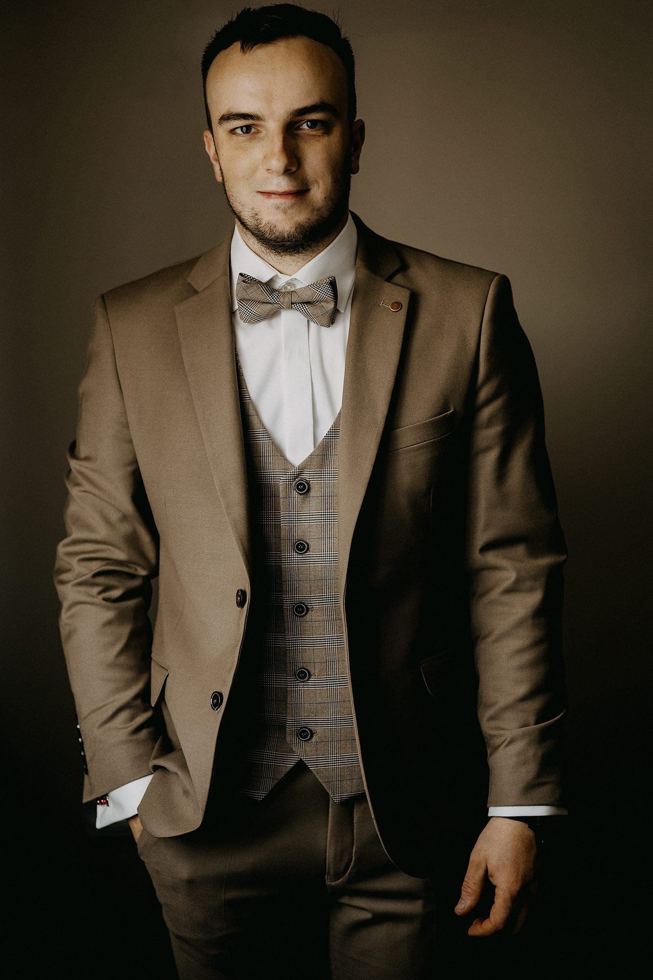 Elegant groom in a taupe three-piece suit with bow tie posing for a formal wedding portrait.