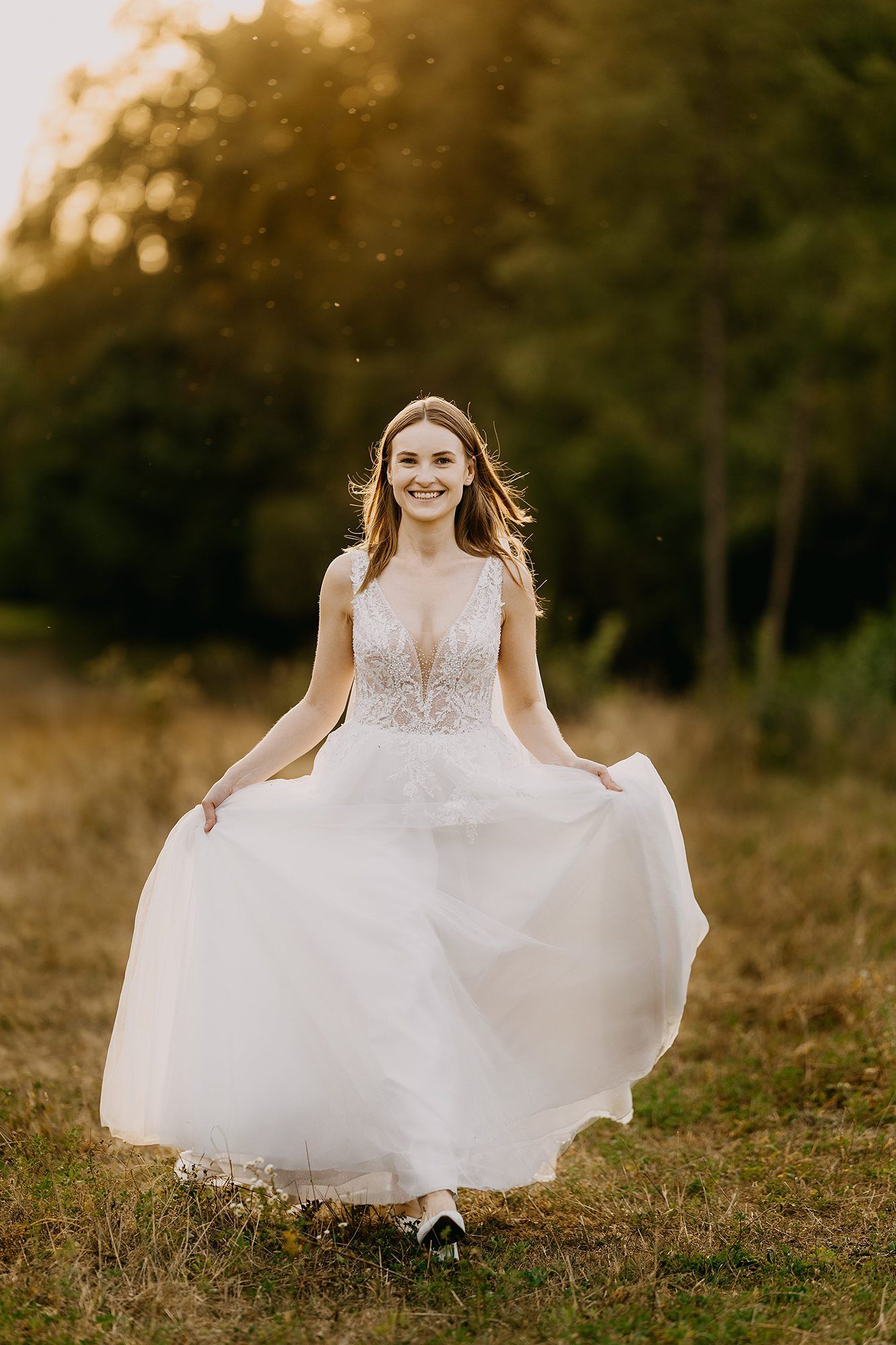 Radiant bride in a lace wedding gown twirling in a sunlit meadow at golden hour.