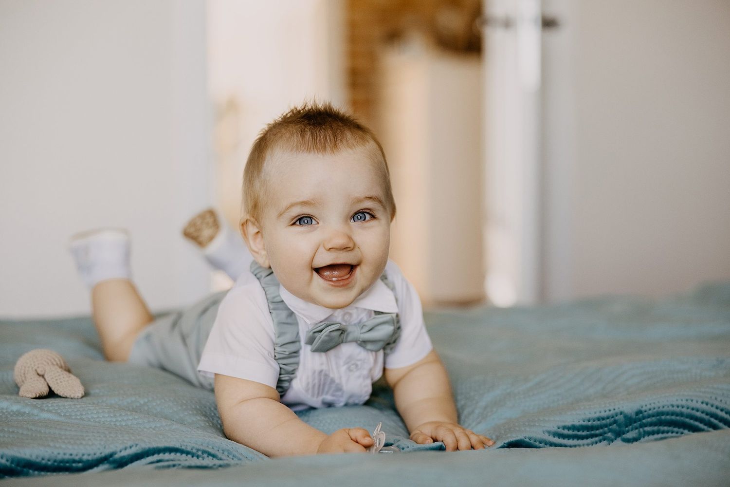 Happy smiling baby in white shirt and bow tie outfit lying on teal blanket during baptism day.