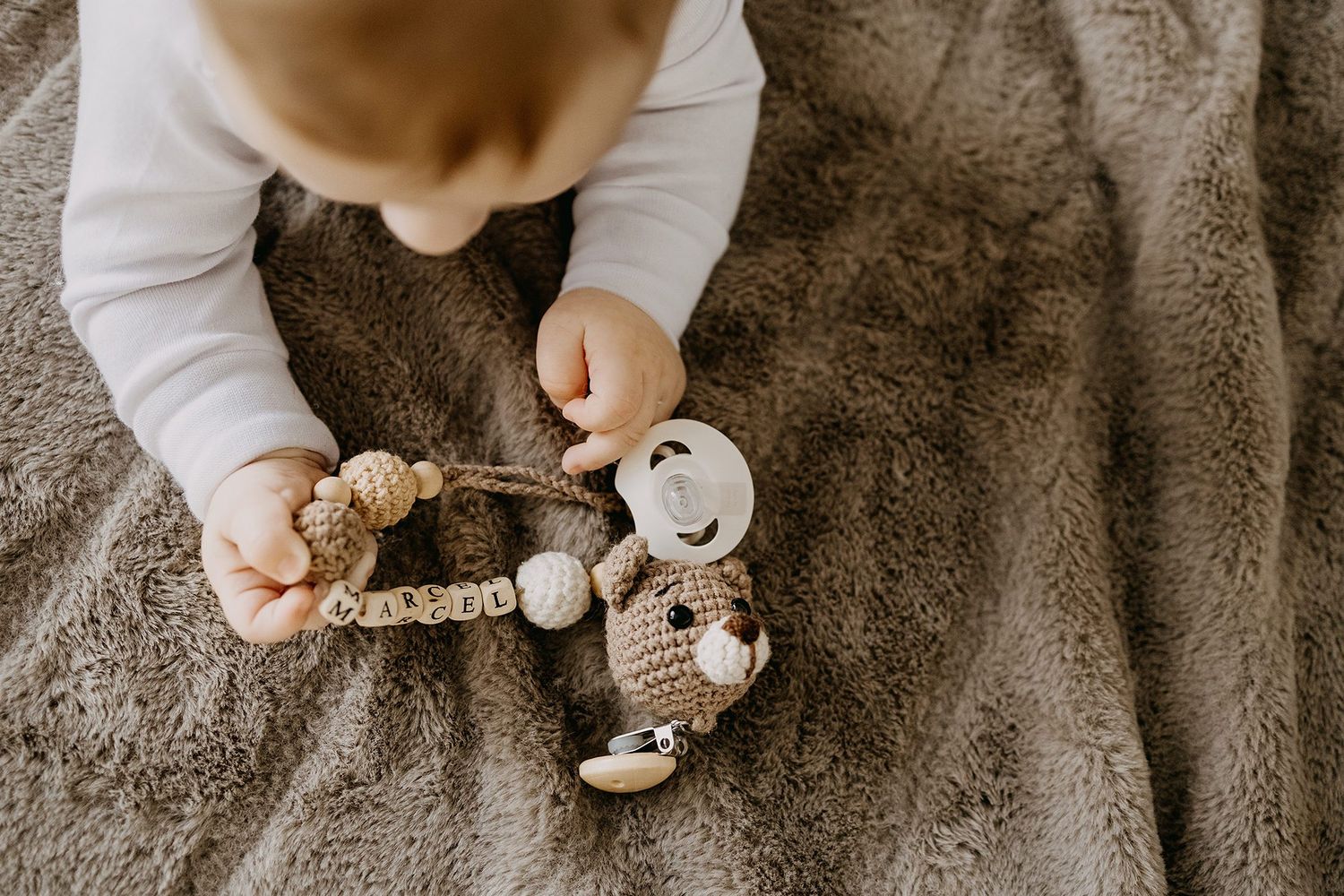 Close-up of a baby reaching for a personalized crocheted teddy bear toy on a soft blanket.