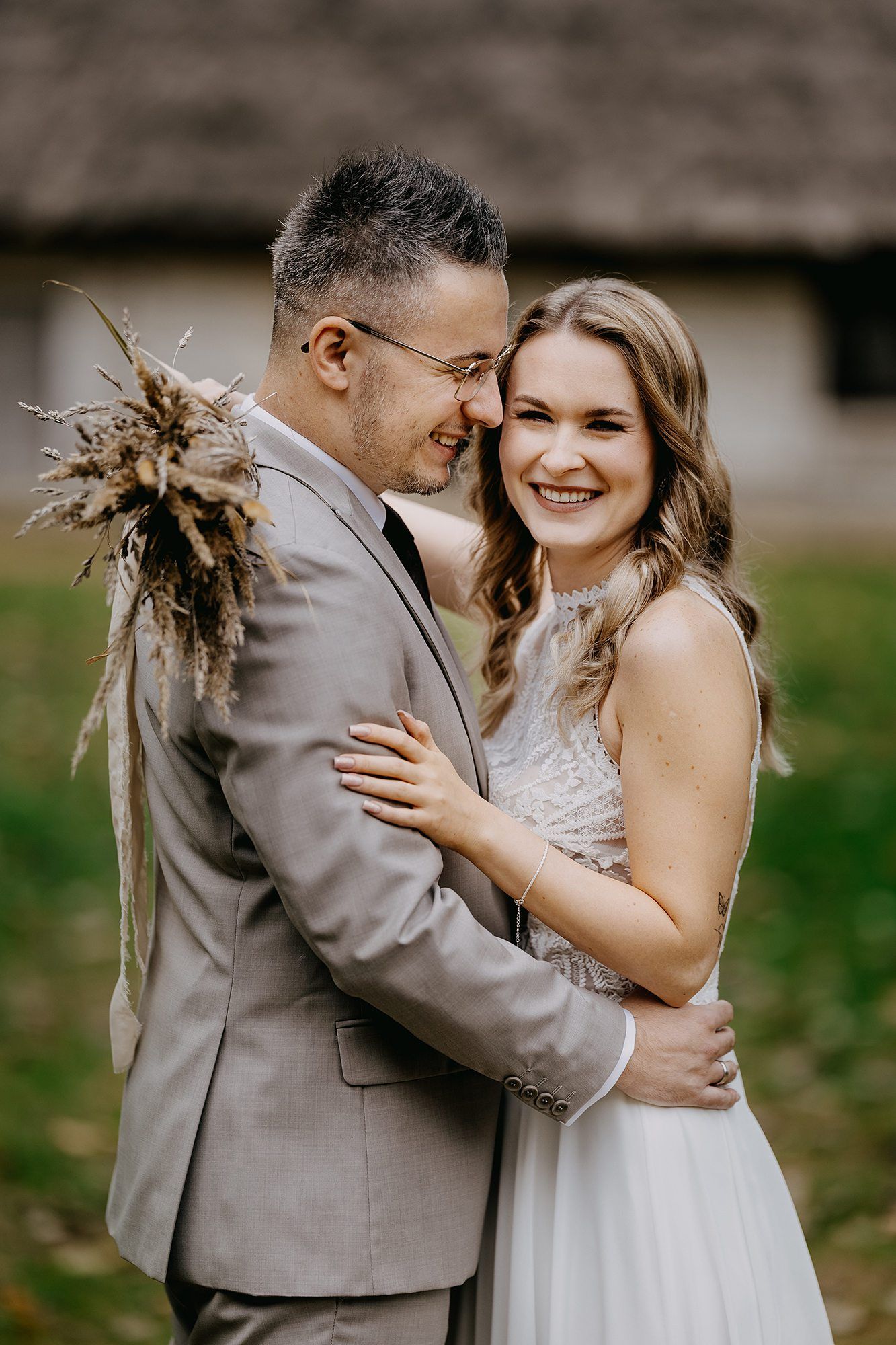 Smiling bride and groom in a close embrace wearing boho-style wedding attire outdoors.