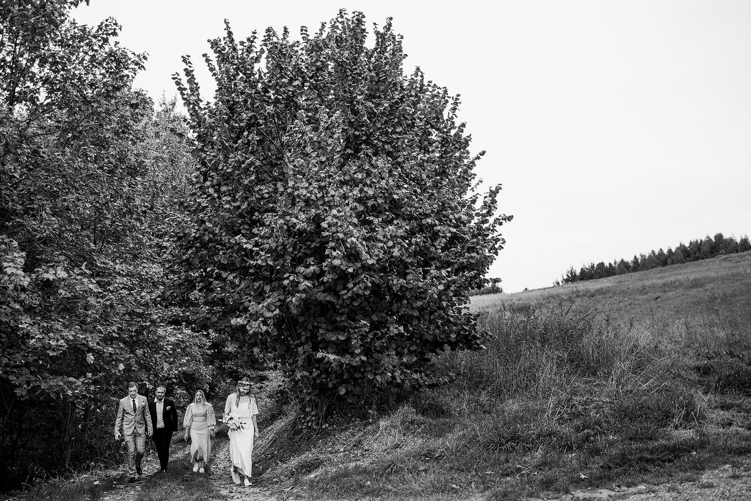 Black and white photo of a small group walking along a tree-lined countryside path.