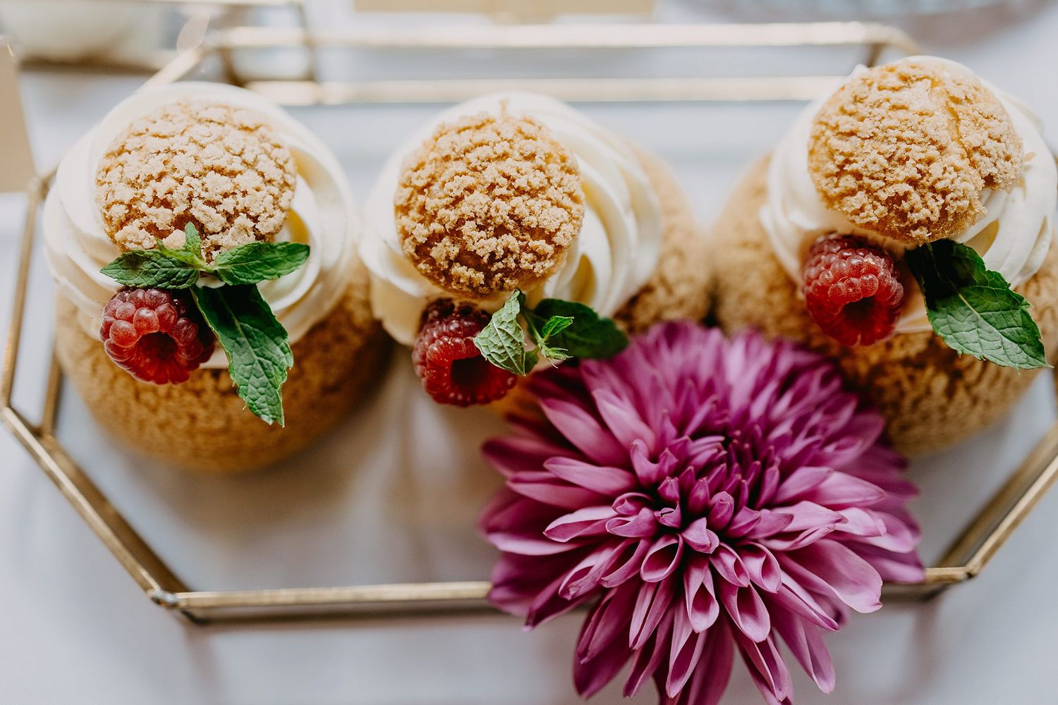 Elegant dessert cups with cream, raspberries, and mint on decorative tray.