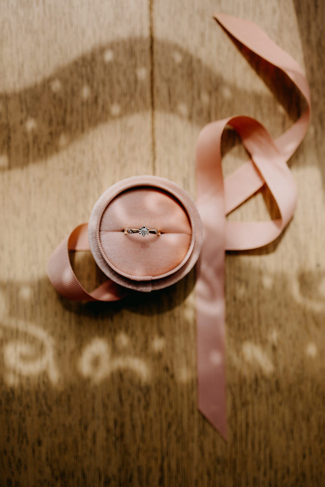 Diamond engagement ring in pink velvet box with satin ribbon on wooden surface.