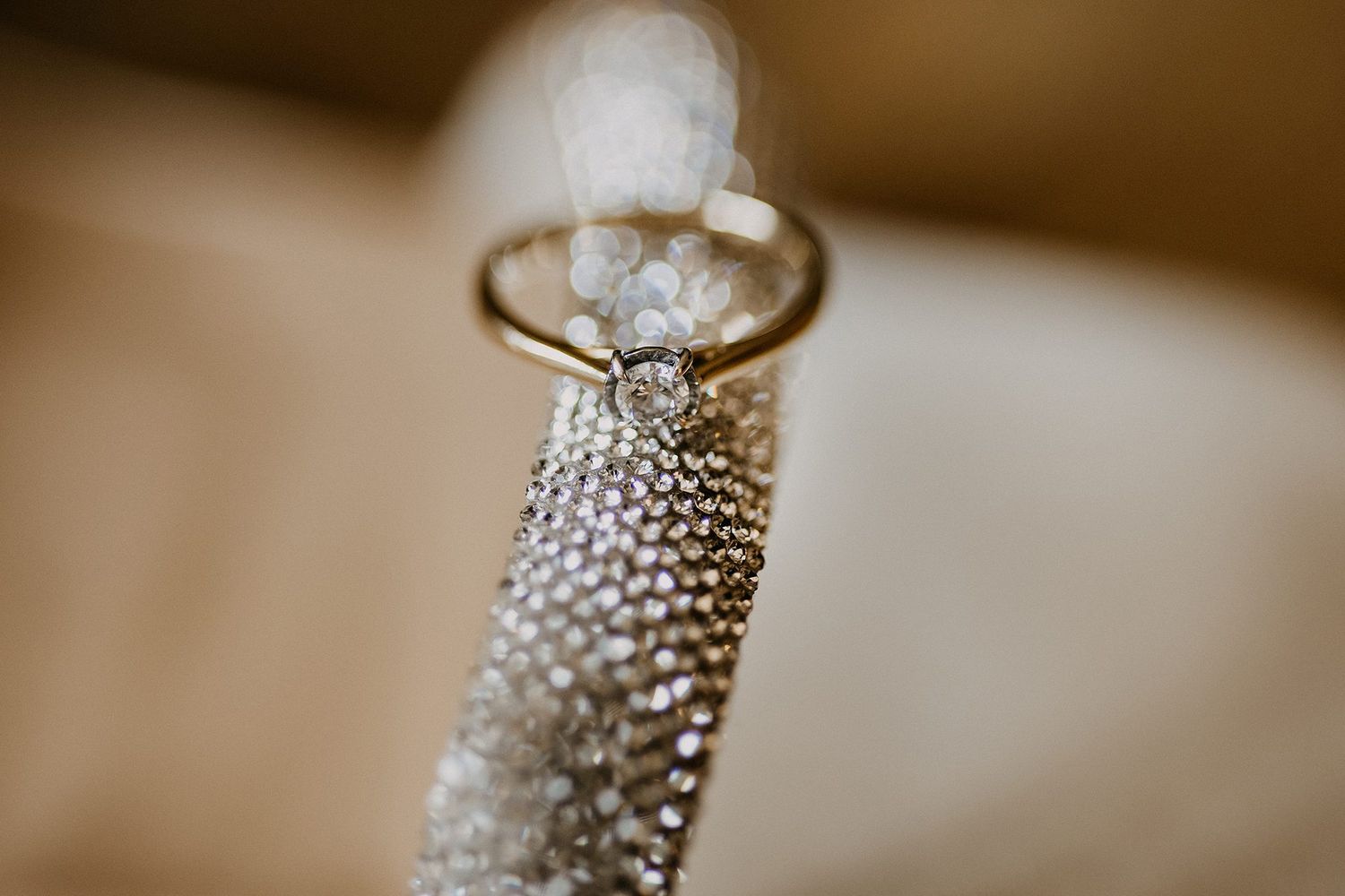 Gold engagement ring with diamond solitaire displayed on textured silver mesh fabric with soft bokeh background.
