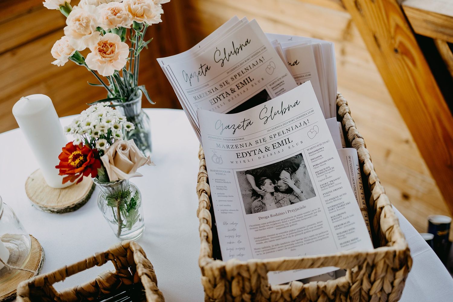 Wedding programs displayed in a wicker basket on a white table with colorful floral arrangements.