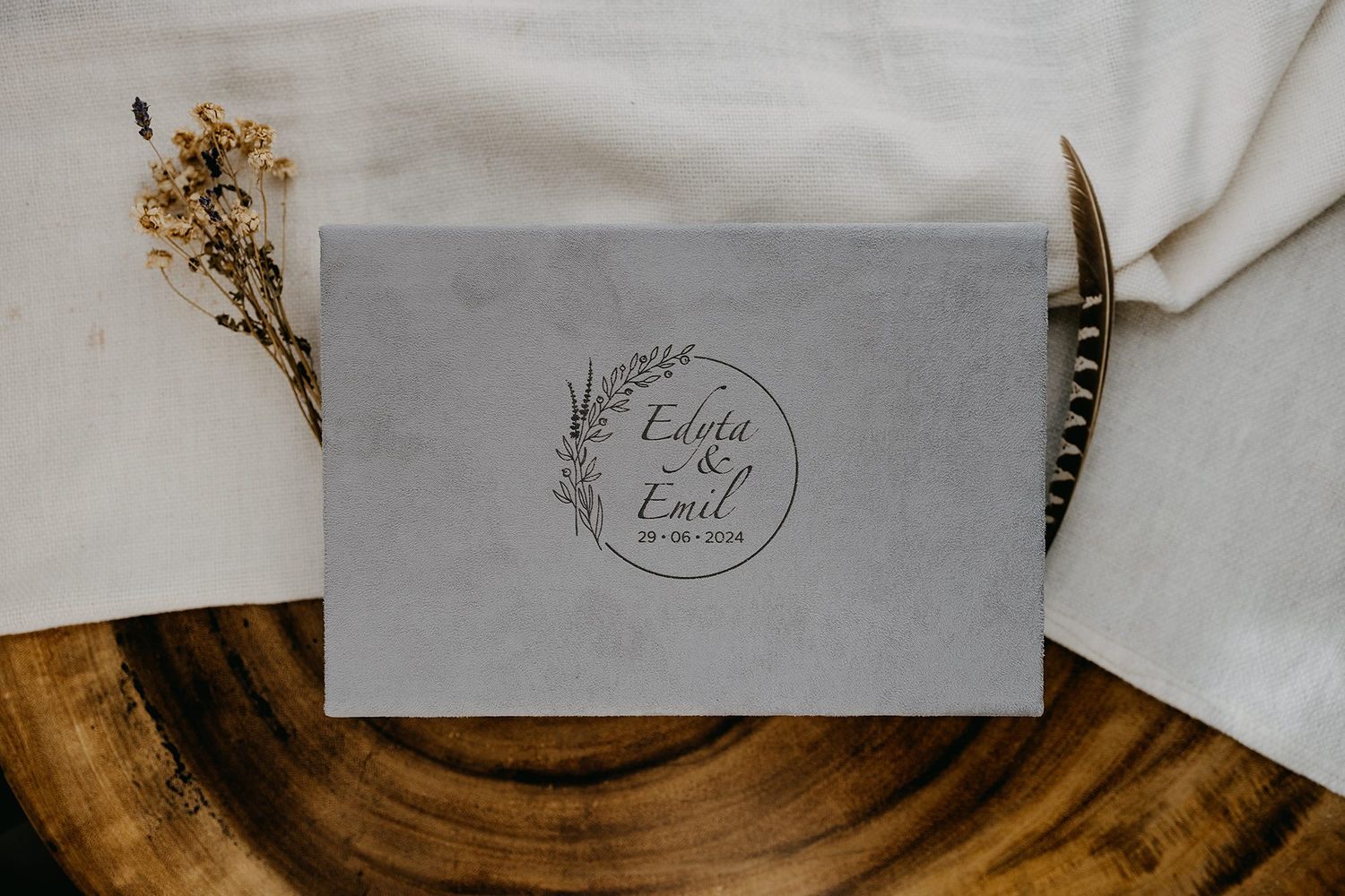 Elegant gray wedding invitation with botanical wreath design featuring names Edyta and Emil on wooden surface.