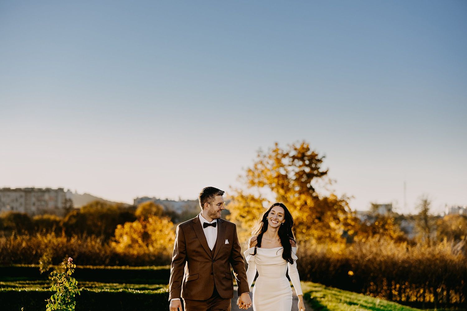 Bride and groom laughing while walking through autumn vineyard landscape.