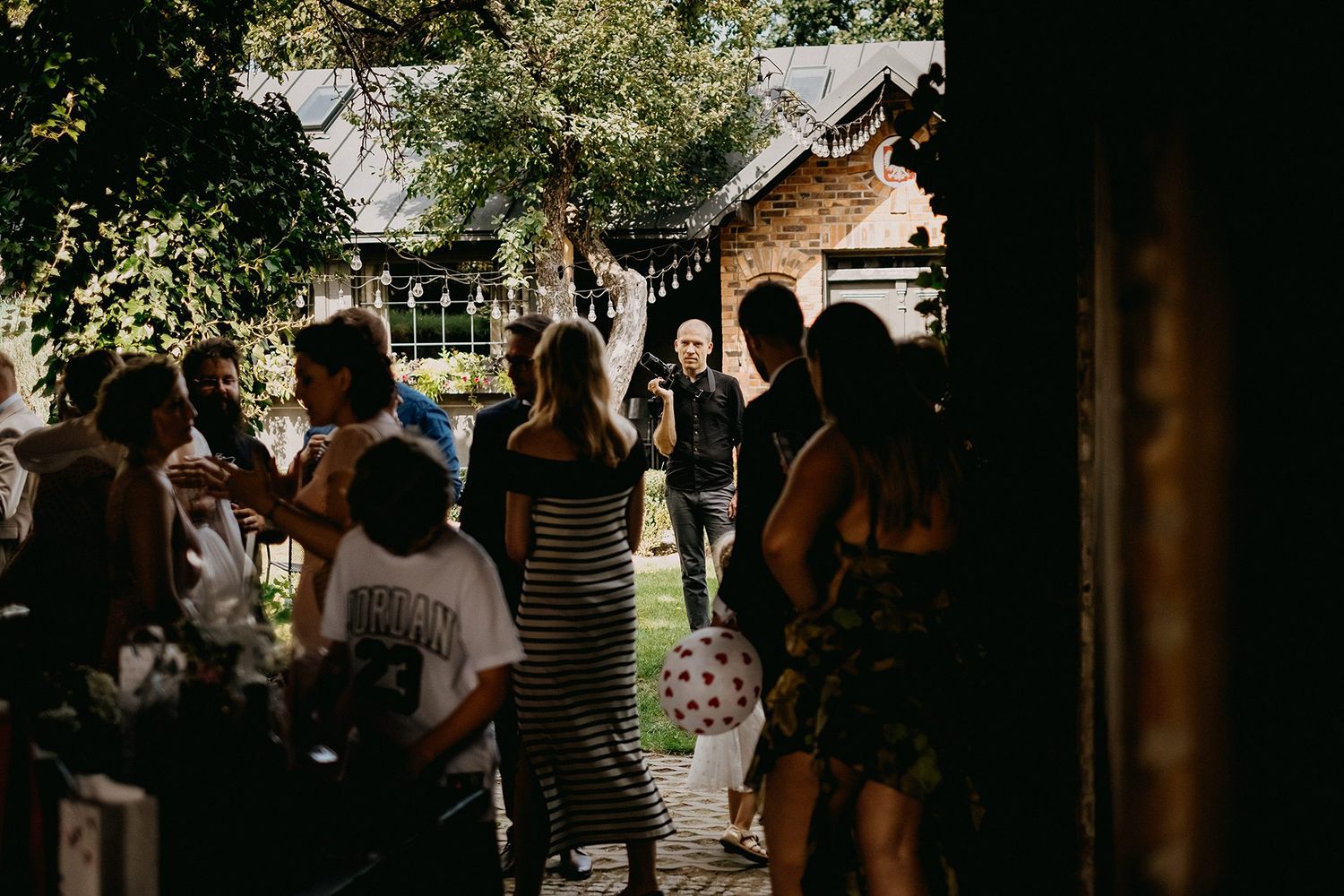 Group of guests gathered outside rustic brick venue on sunny day.