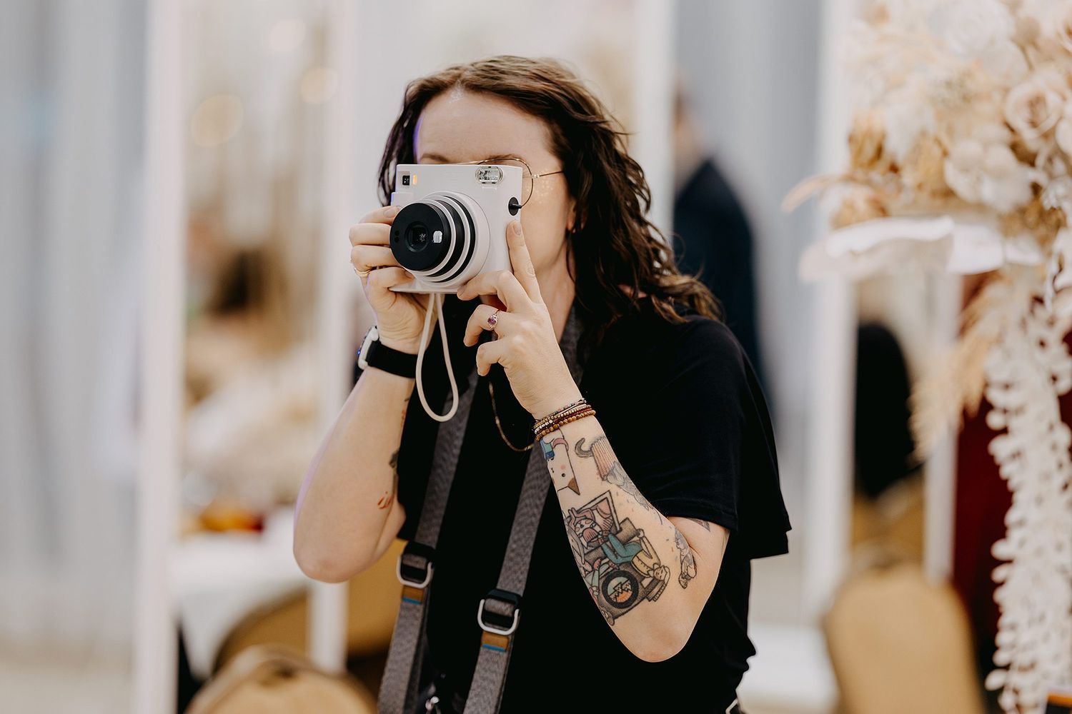 Tattooed woman taking a selfie with a vintage instant camera in a bright decorated interior.
