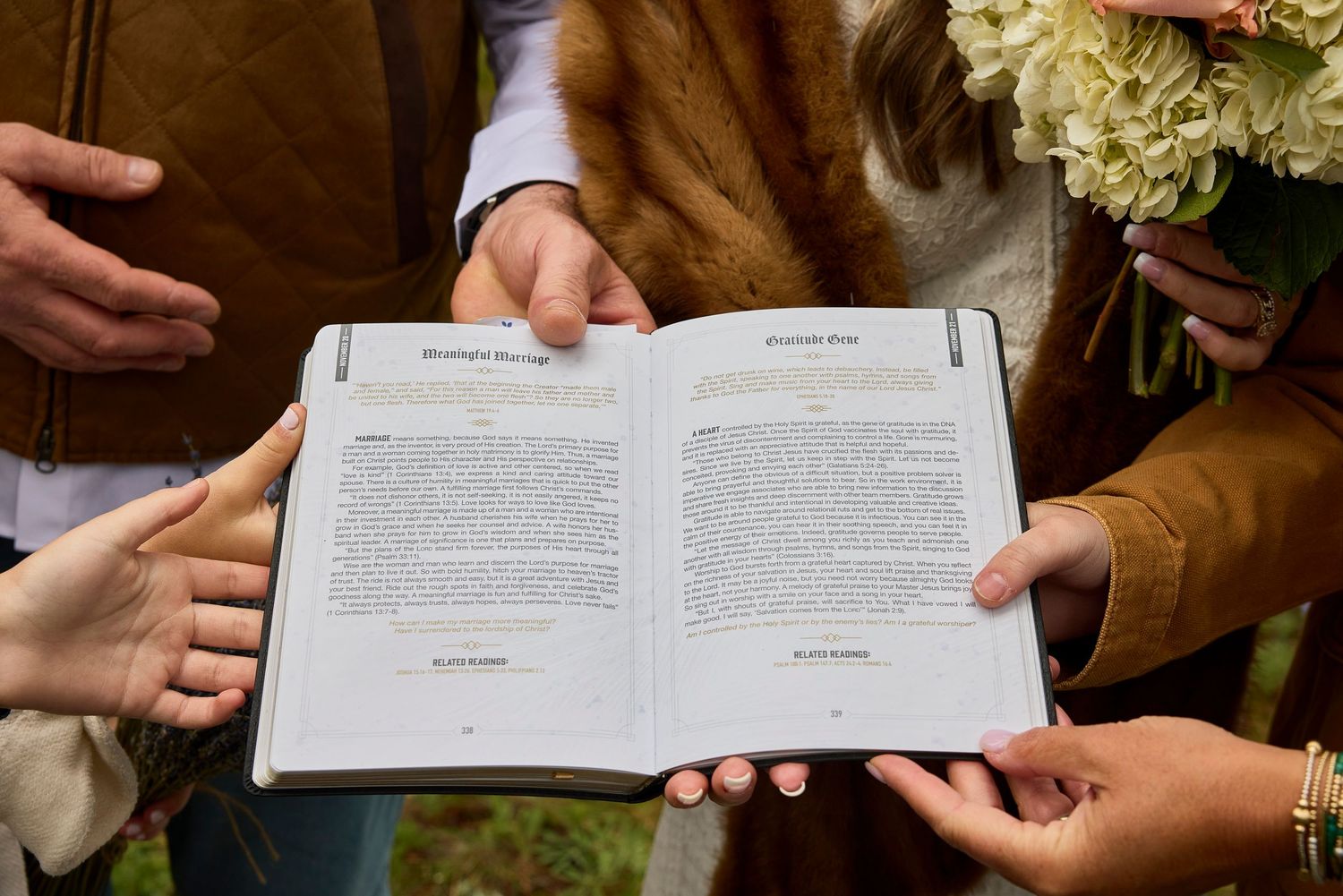 Couple and guests placing hands on open Bible during outdoor woodland wedding ceremony.