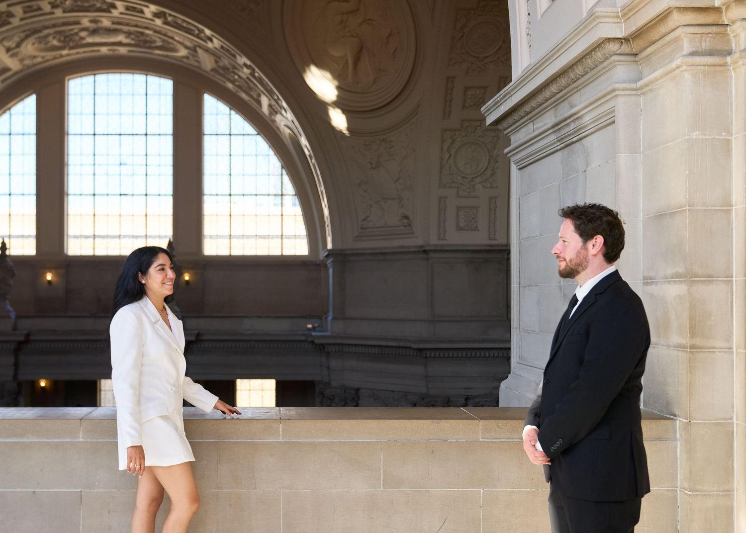 Couple sharing a tender moment in San Francisco City Hall, bride in white blazer dress and groom in black suit.