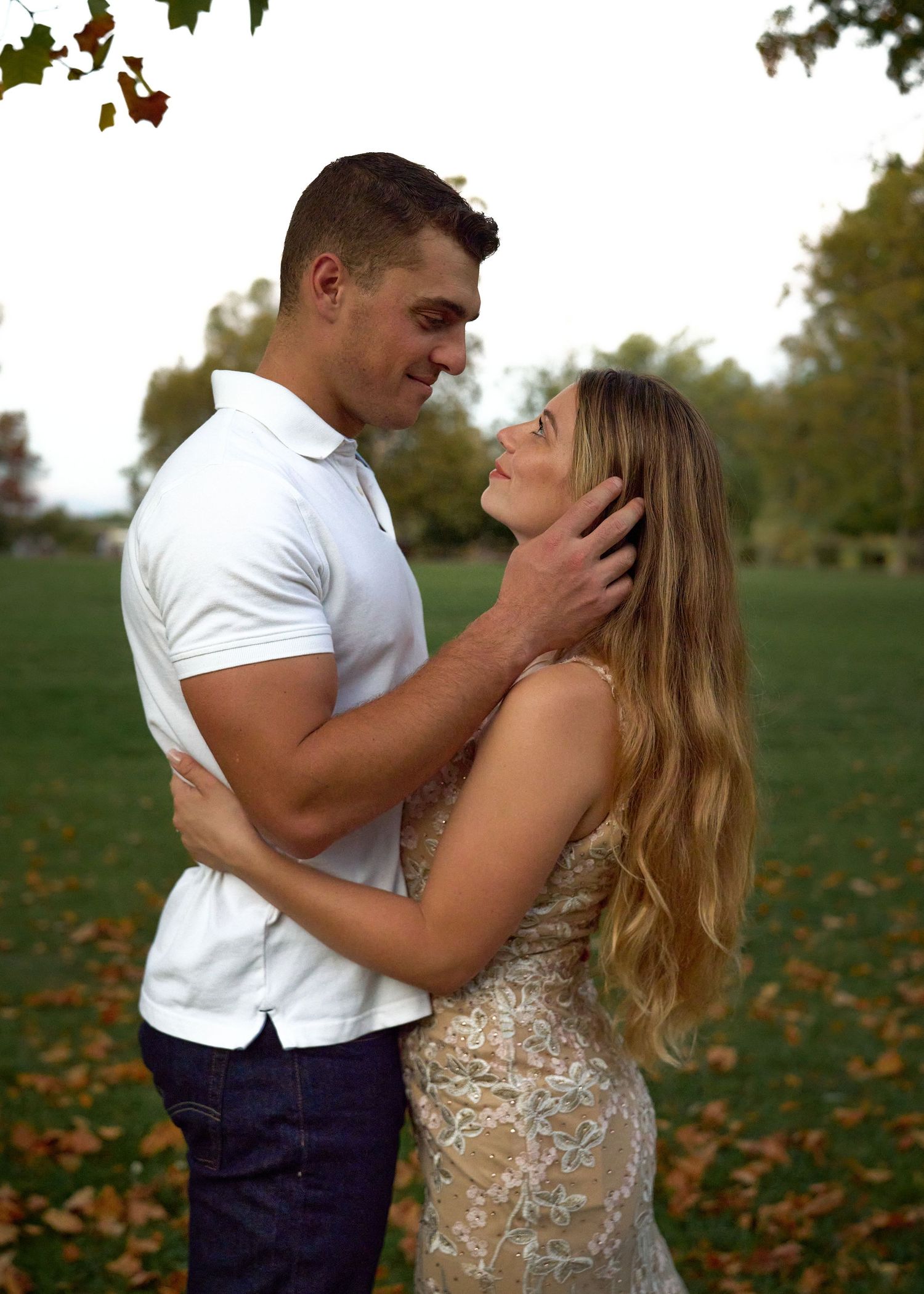 Romantic couple in lace dress and white shirt gazing at each other in autumn park setting.
