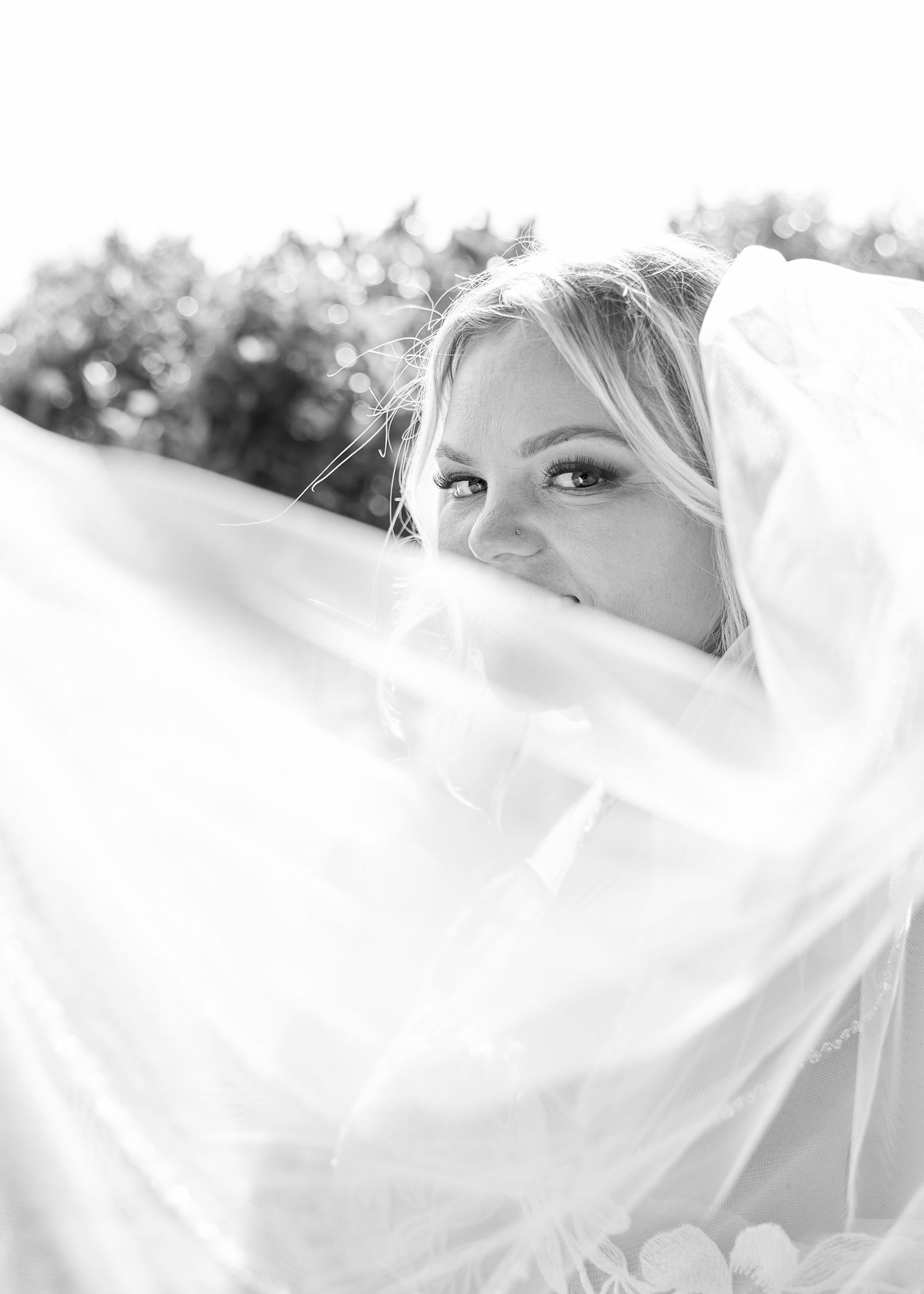 Beautiful blonde bride peeks through her flowing veil in a dreamy black and white bridal portrait.