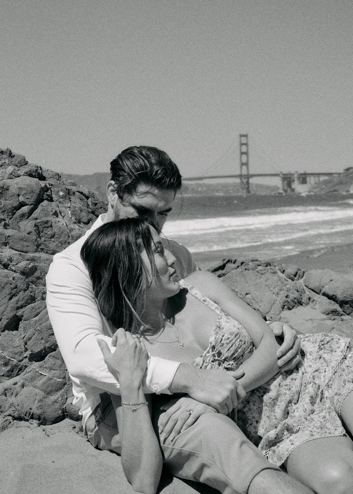 Black and white photo of couple in a tender moment on rocky Baker Beach.