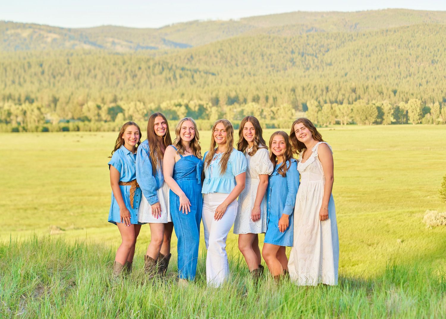 Six young women in coordinating blue and white outfits posing in sunlit mountain meadow.