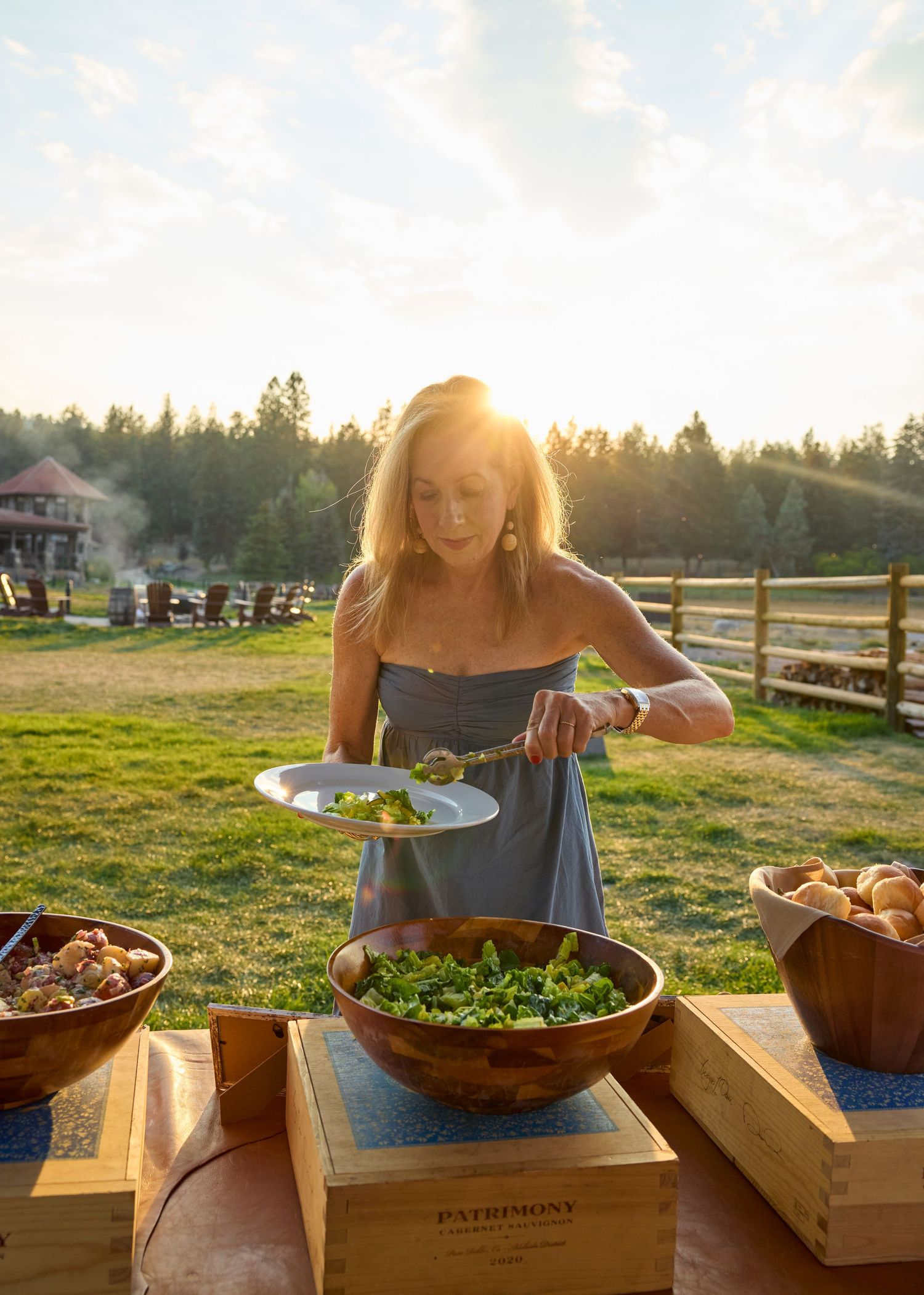 Woman serving fresh kale salad at an outdoor farm-to-table dinner event during golden hour sunset.
