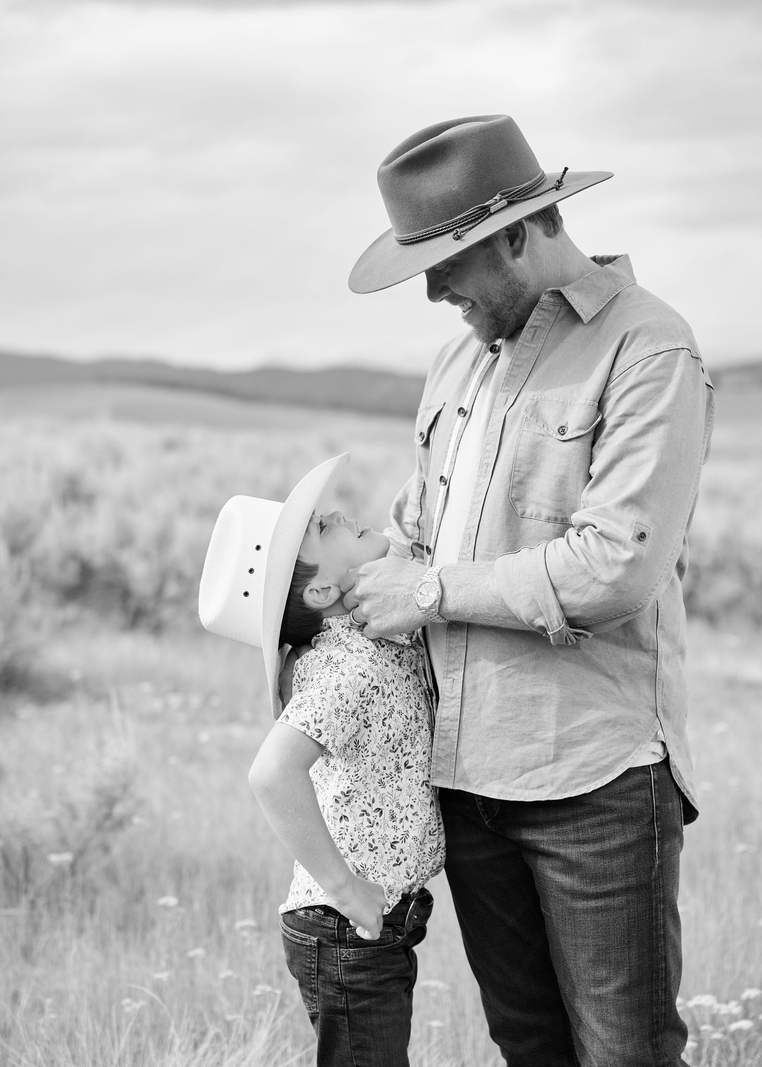 Black and white photo of father in cowboy hat bonding with young child in open field.