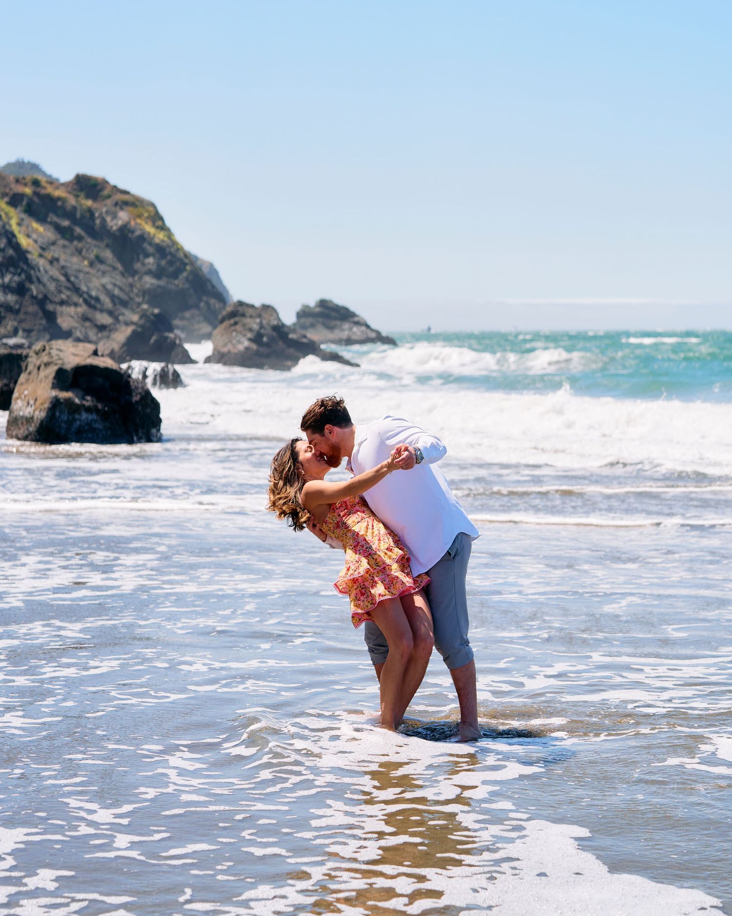 Couple sharing a romantic kiss in ocean waves on a sunny California beach.