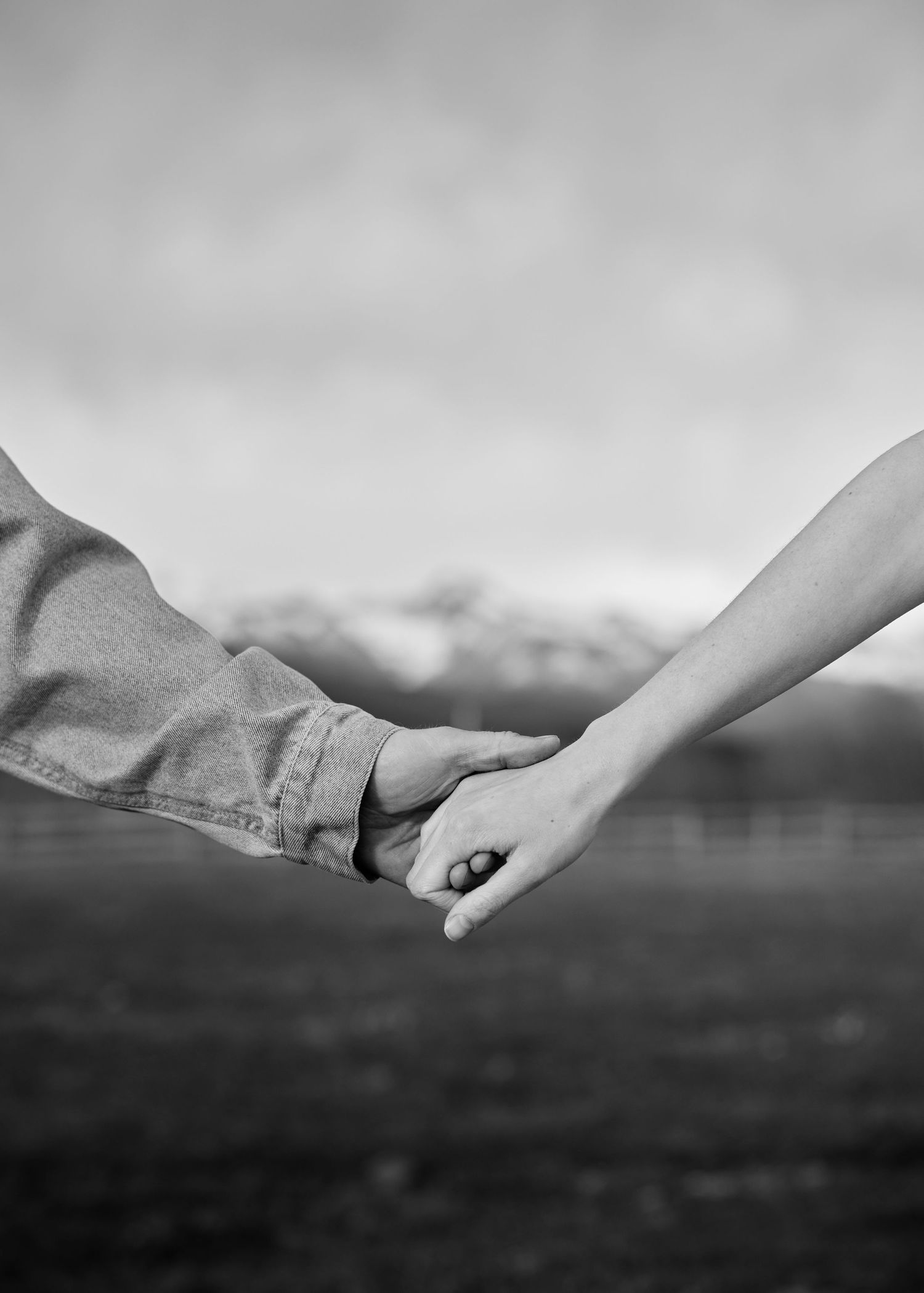 Black and white close-up of couple holding hands in front of mountain landscape.