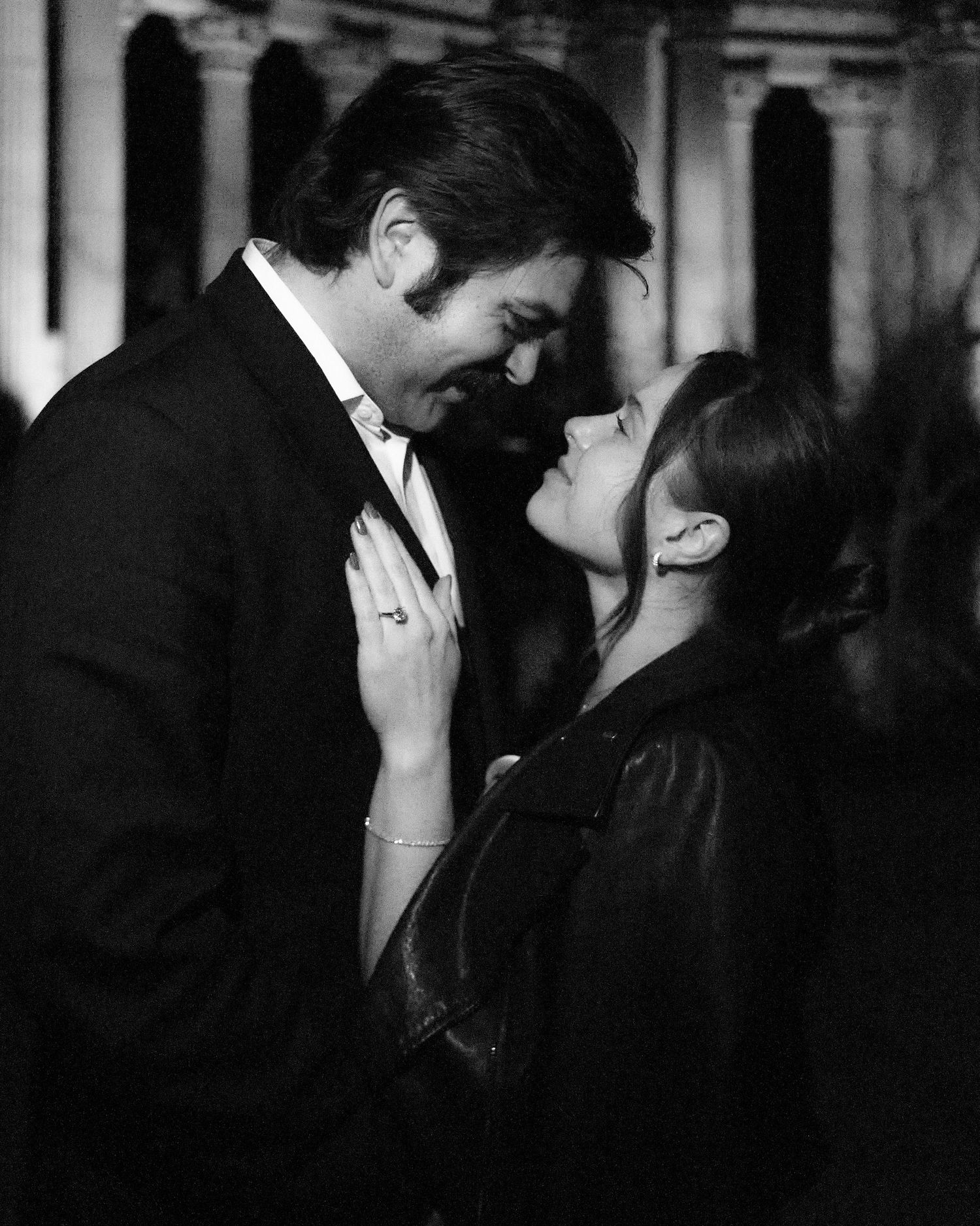 Black and white photo of a romantic couple sharing an intimate moment, almost kissing outdoors at night.