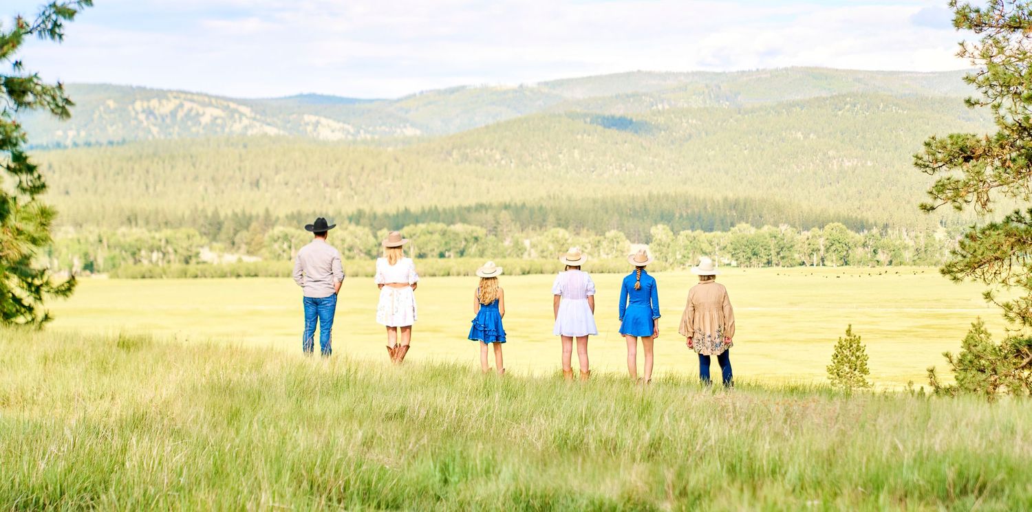 Group of six people standing together viewing a scenic mountain meadow landscape from behind.
