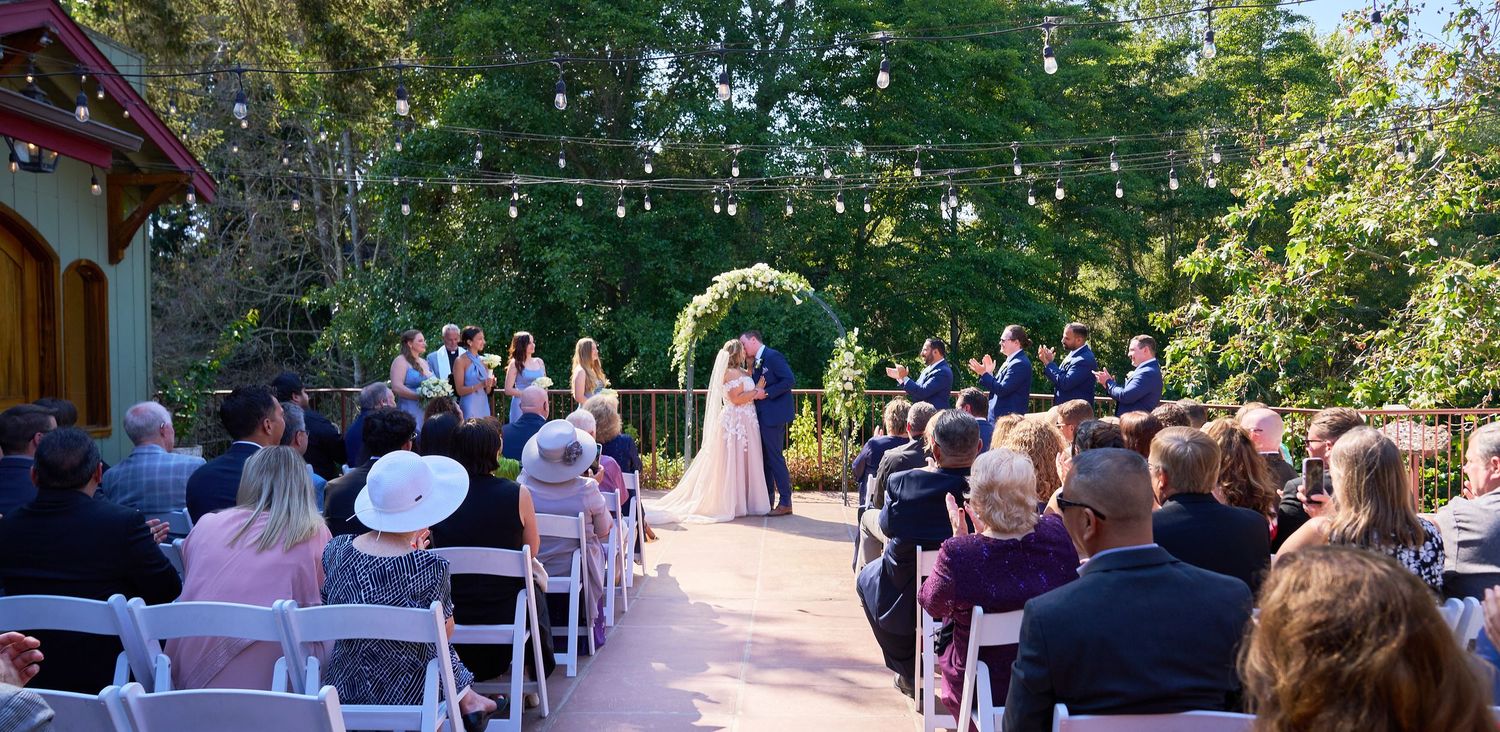 Bride and groom exchange vows at outdoor garden wedding ceremony with string lights and seated guests.