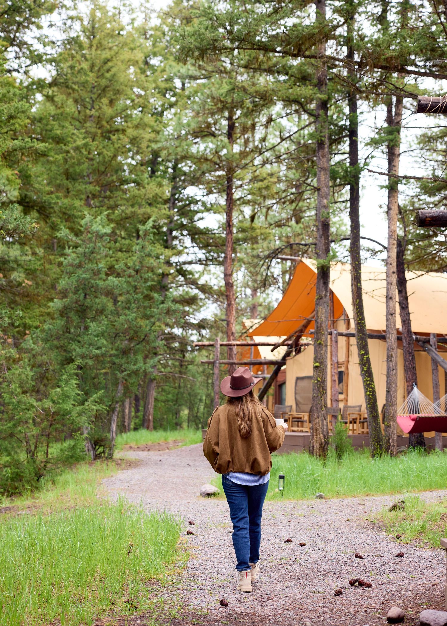 Woman in hat carries a canoe toward a glamping tent along a forest path.
