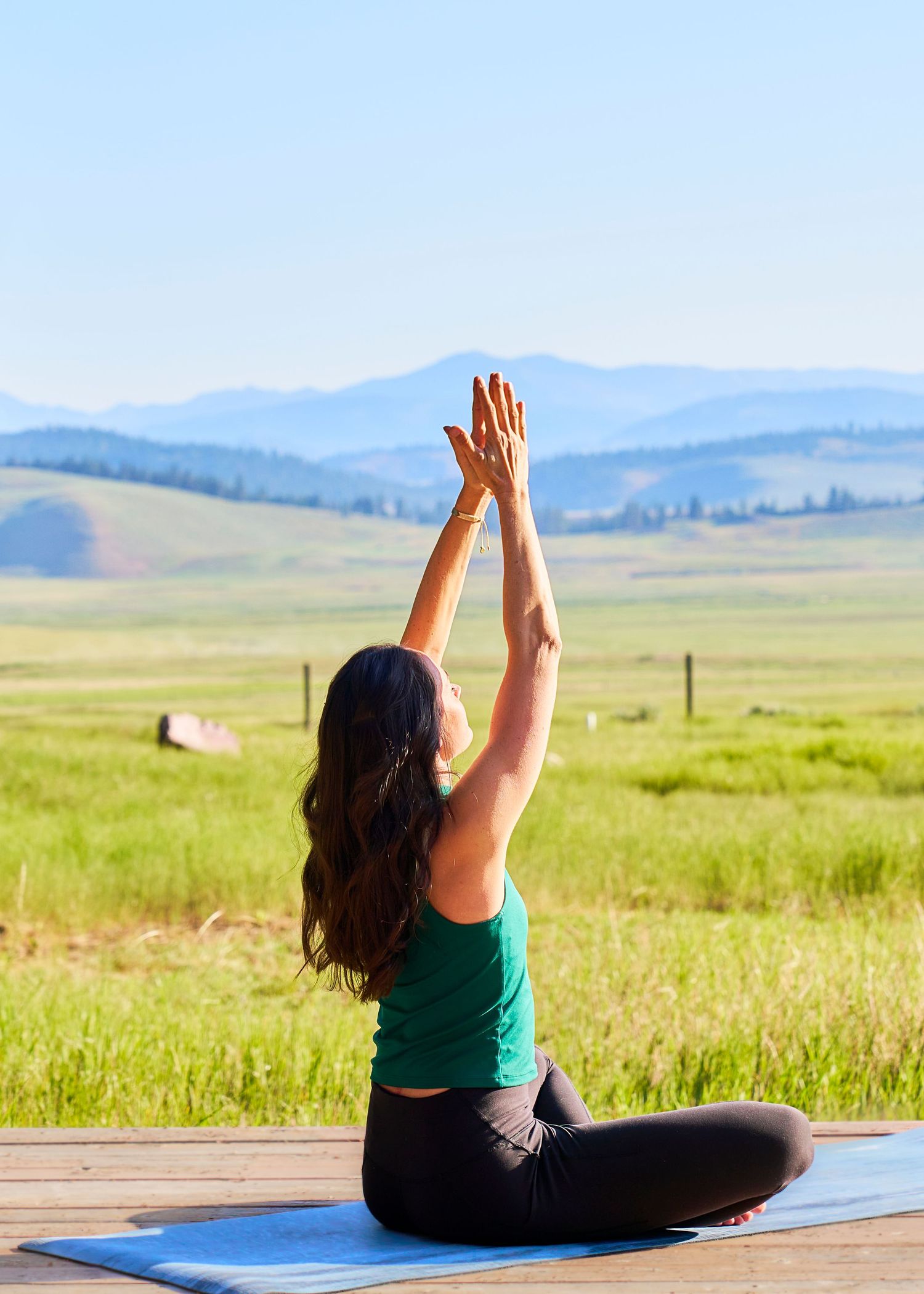 Woman doing yoga outdoors on a blue mat overlooking green fields and mountains.
