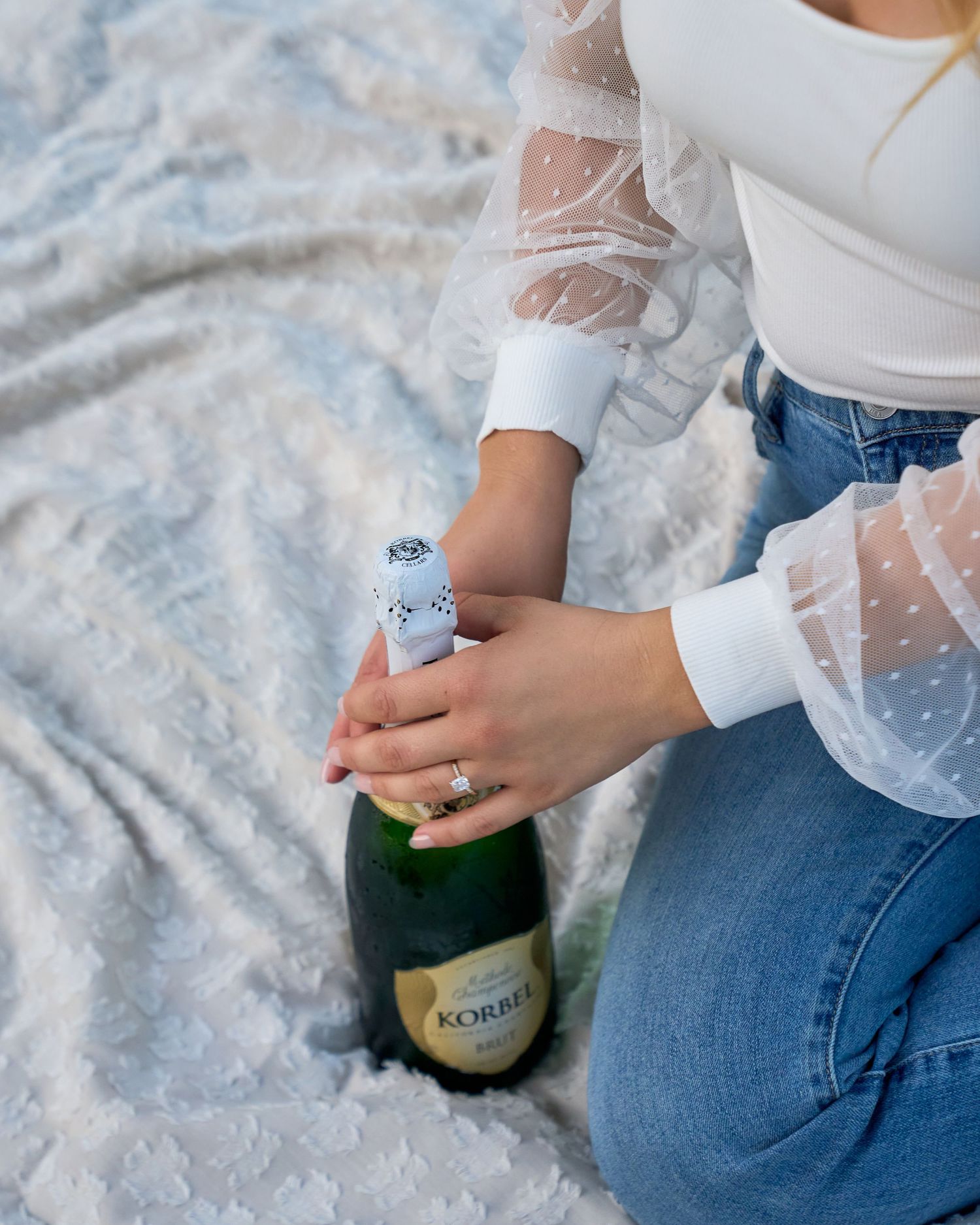 Woman in white lace top opening a Korbel champagne bottle during engagement celebration.
