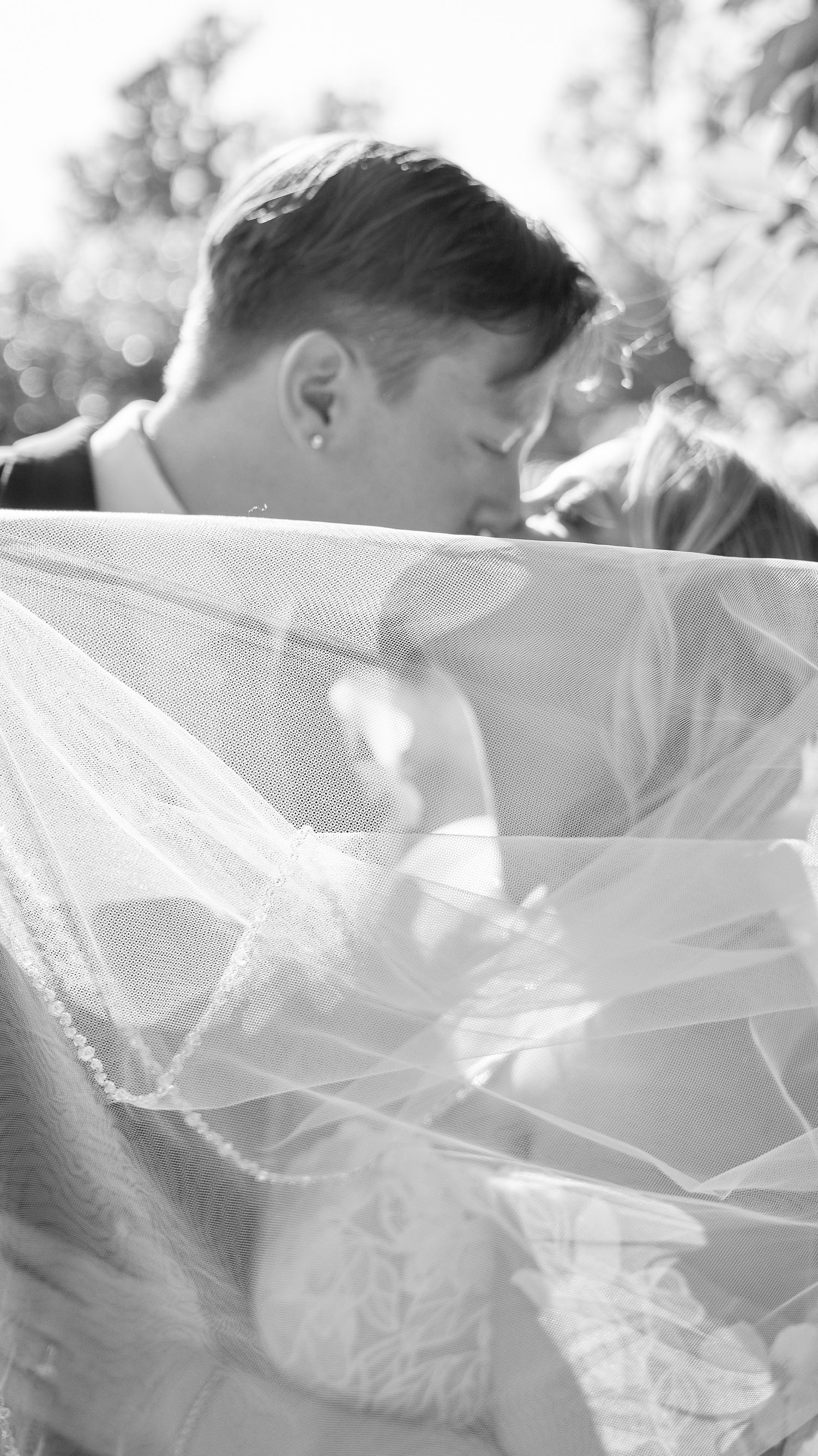Romantic black and white photo of bride and groom kissing beneath flowing wedding veil.