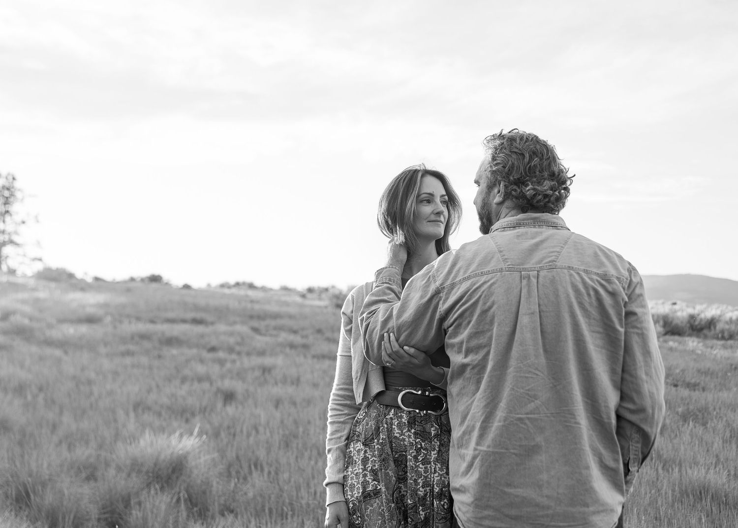 Black and white photo of a couple sharing a tender moment in a grassy field.