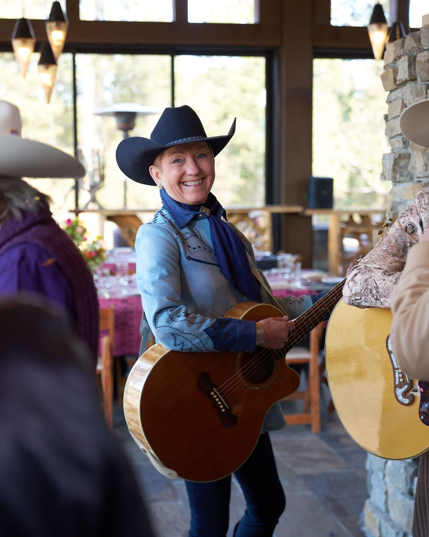 Smiling musician in cowboy hat playing acoustic guitar at an indoor western-themed dining event.