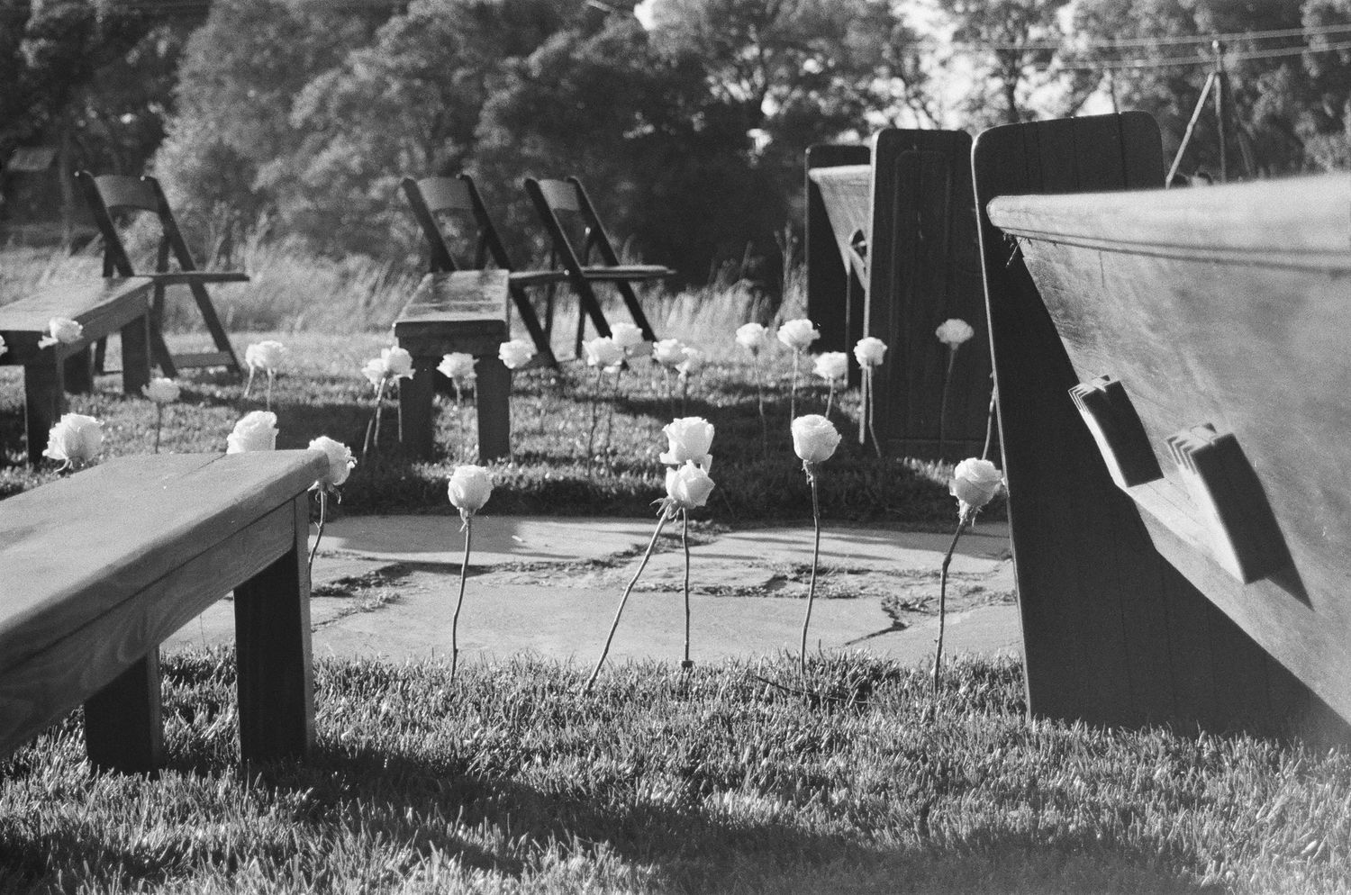 Black and white photo of white flower decorations on tall stems in a grass wedding venue setting.