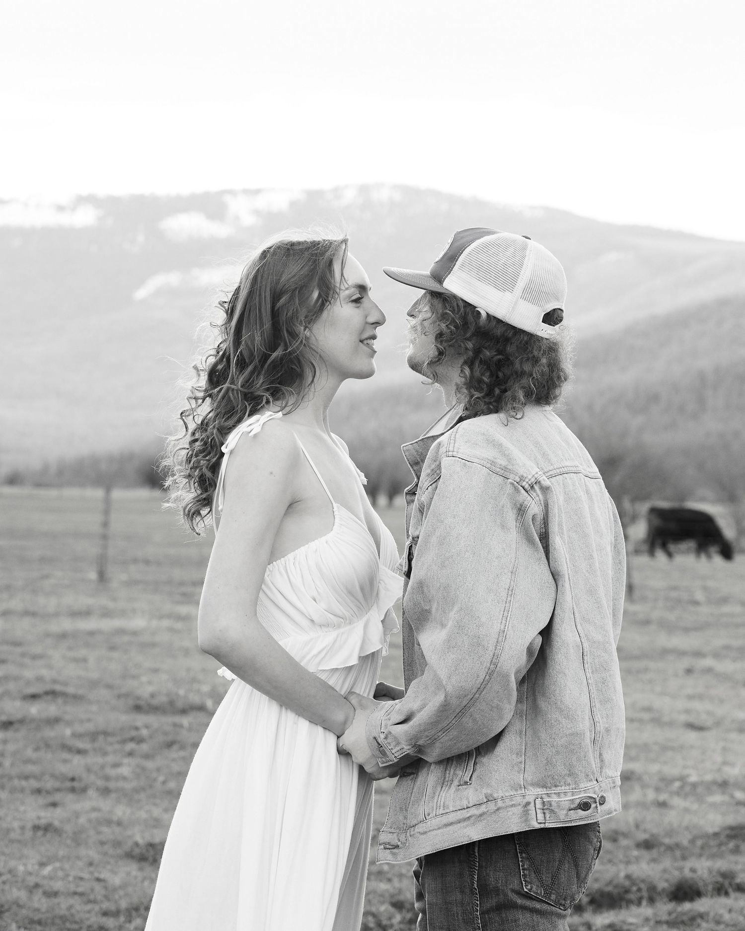 Black and white photo of a couple facing each other, holding hands in a mountain meadow.