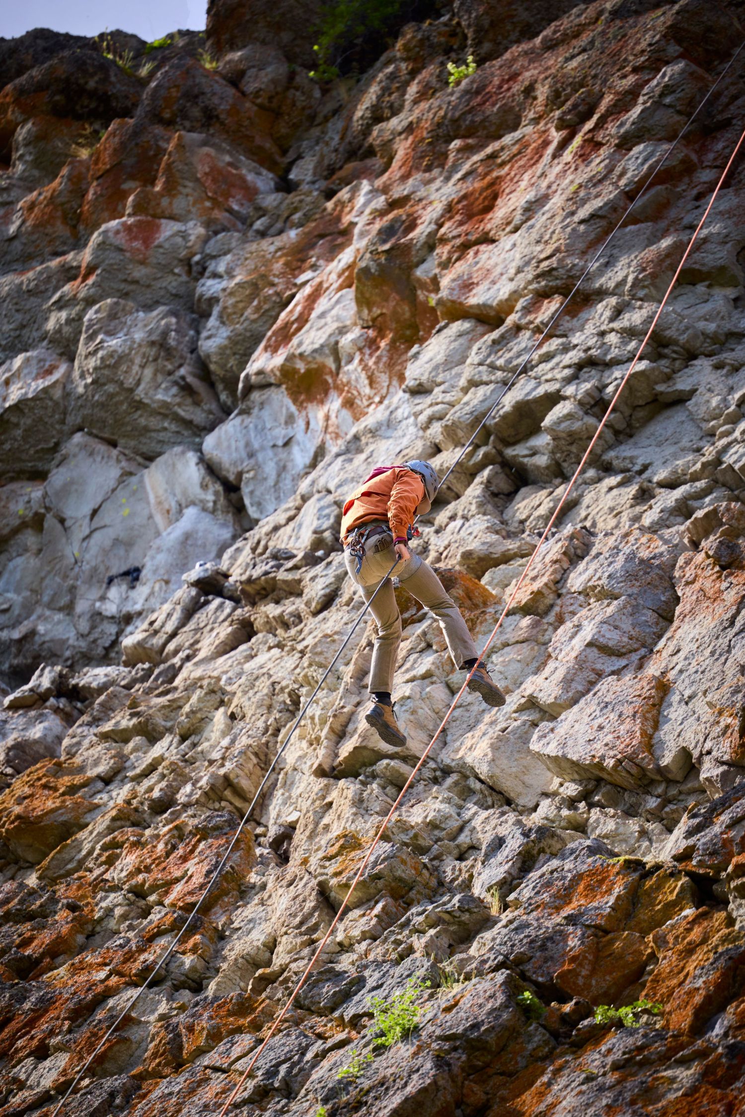 A rock climber scaling a rugged red and gray cliff face using ropes and safety equipment.