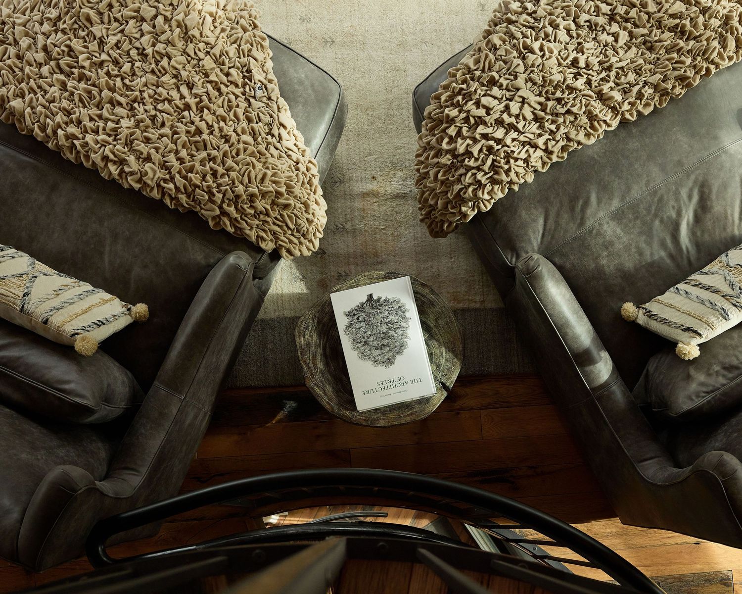 Overhead view of two dark leather armchairs with woven pillows flanking a small round table with a book.