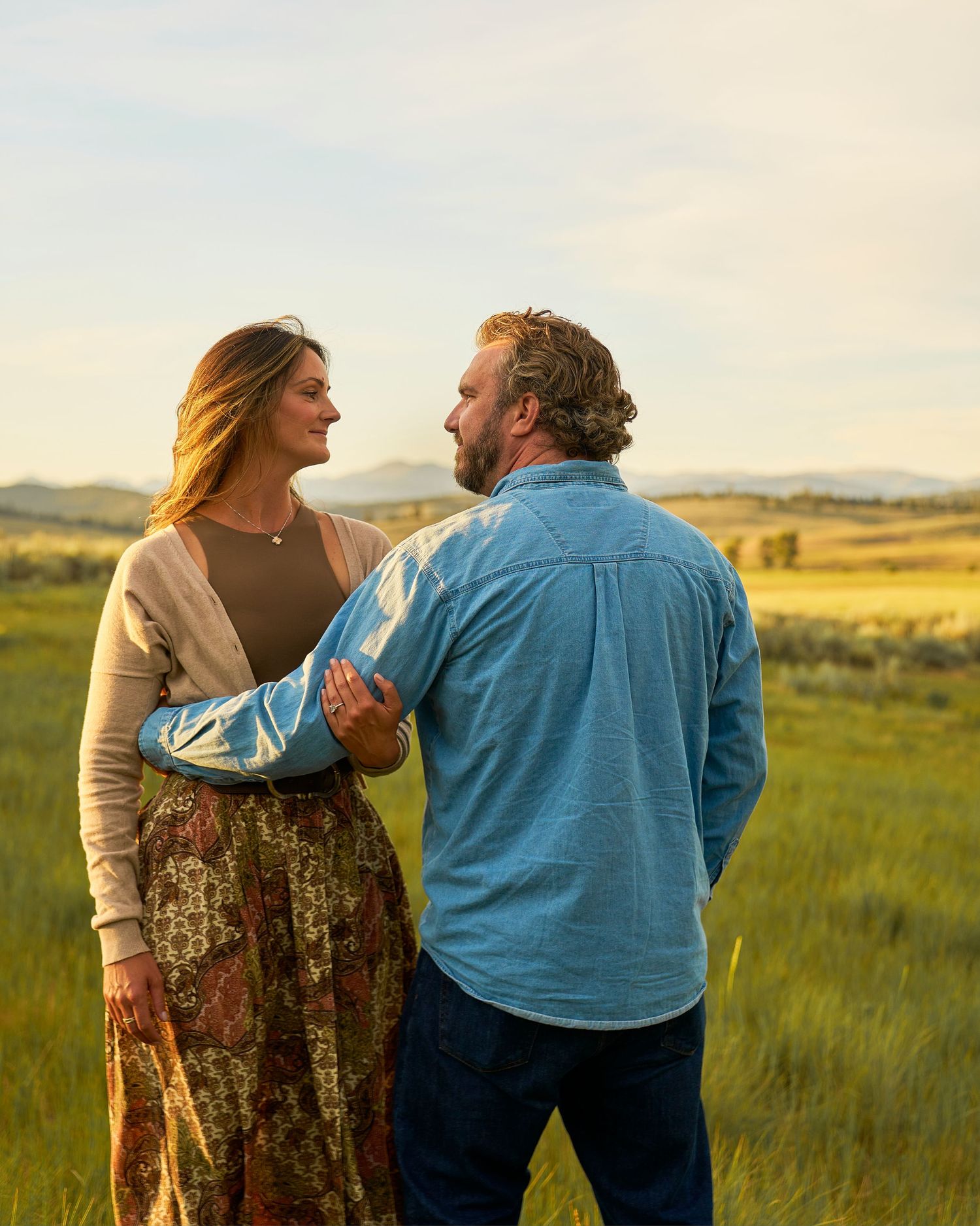 Couple sharing a romantic moment in a lush green field at golden hour, woman wearing floral skirt.