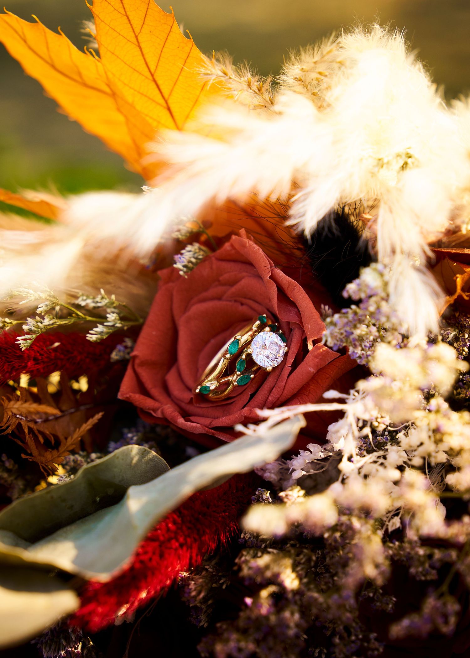 Close-up of a diamond engagement ring resting on a deep red rose surrounded by an autumn wedding bouquet.