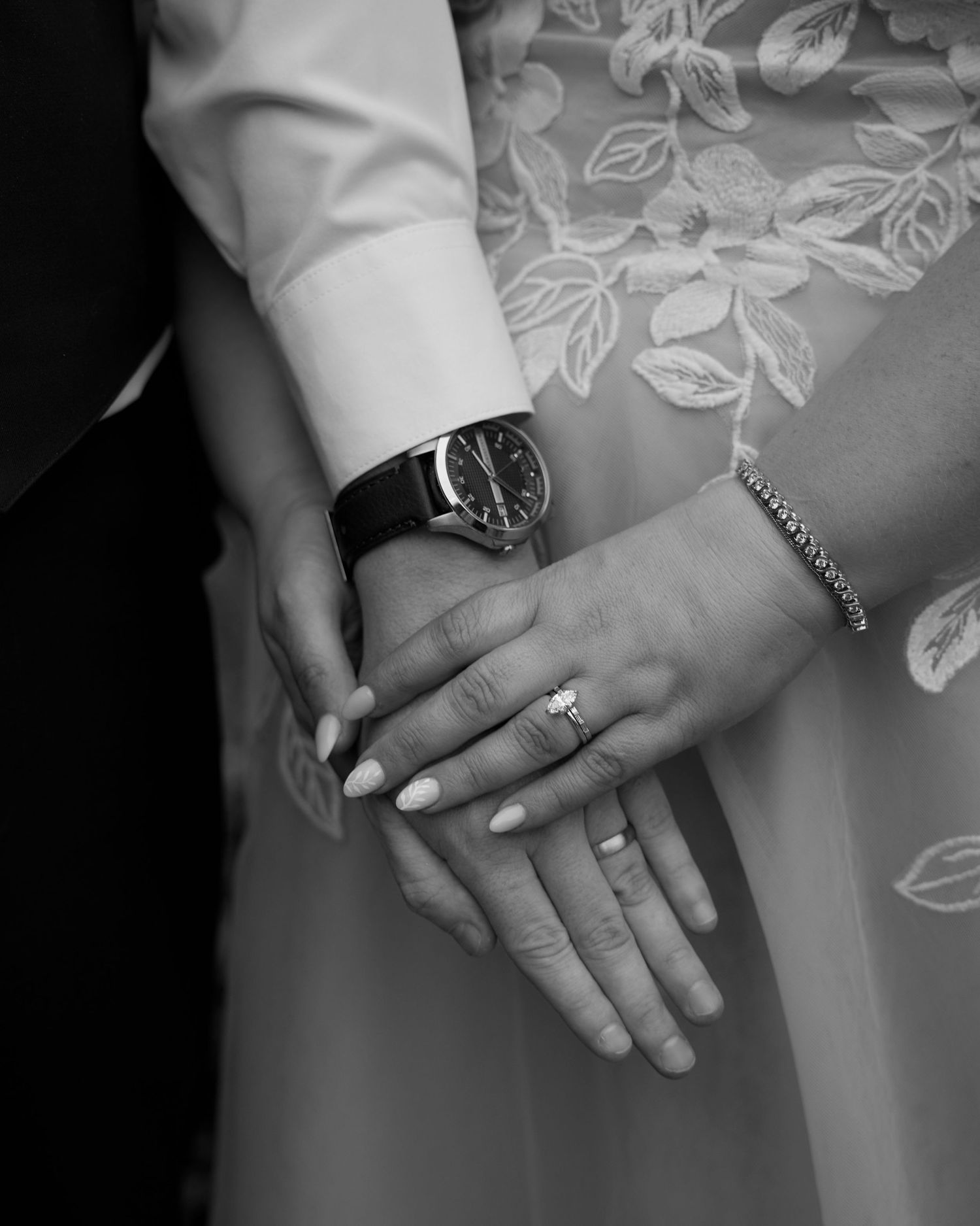 Black and white close-up of bride and grooms hands showing wedding rings and watch.