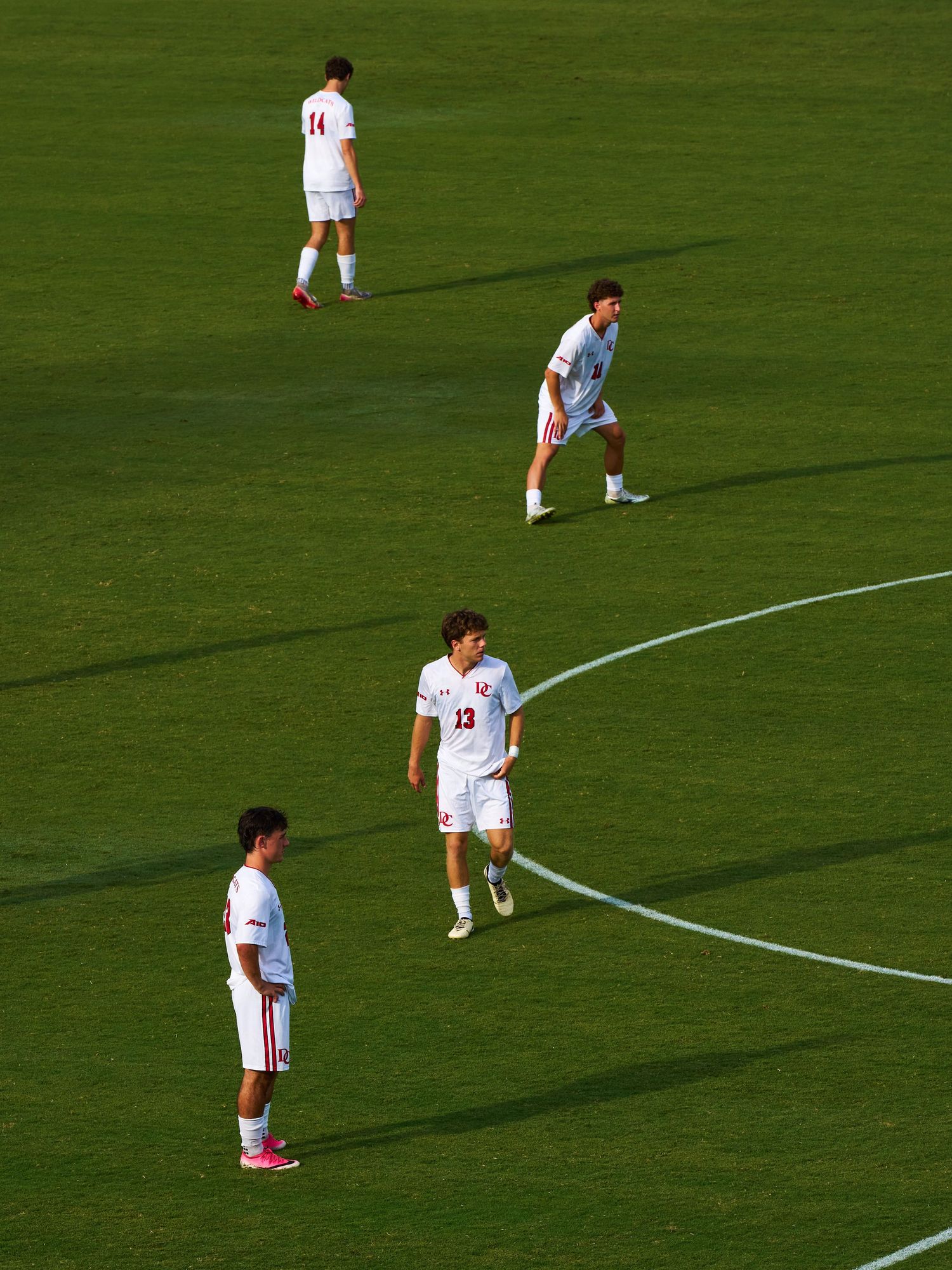 Four soccer players in white uniforms positioned on a green field near the center circle during a match.