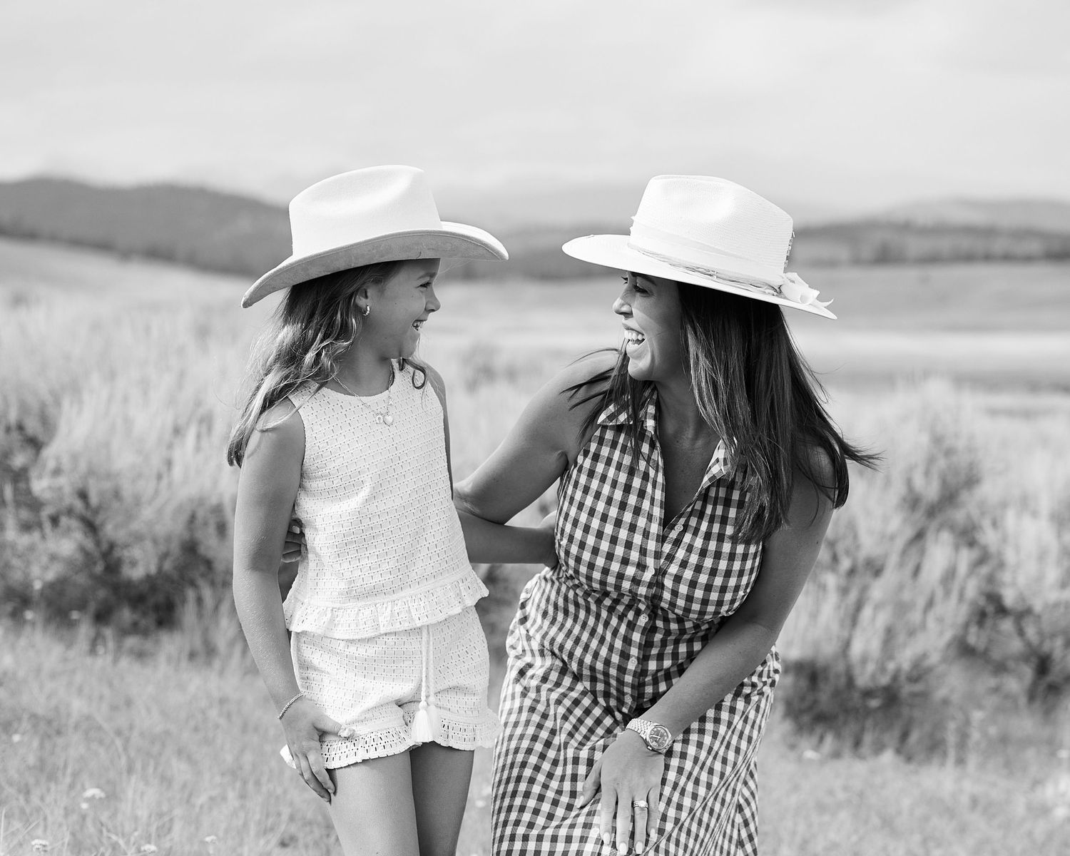 Black and white photo of mother and daughter in matching straw hats smiling at each other.